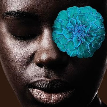 Close-up of a person's face with a blue flower covering one eye against a dark background