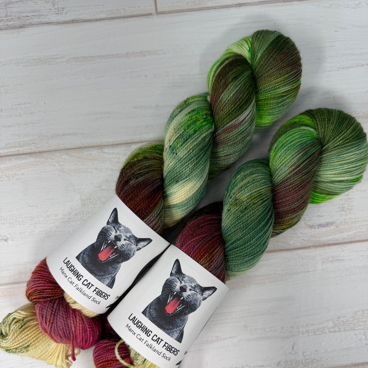 Two skeins of green and red yarn with labels featuring black cats on a light wooden surface.