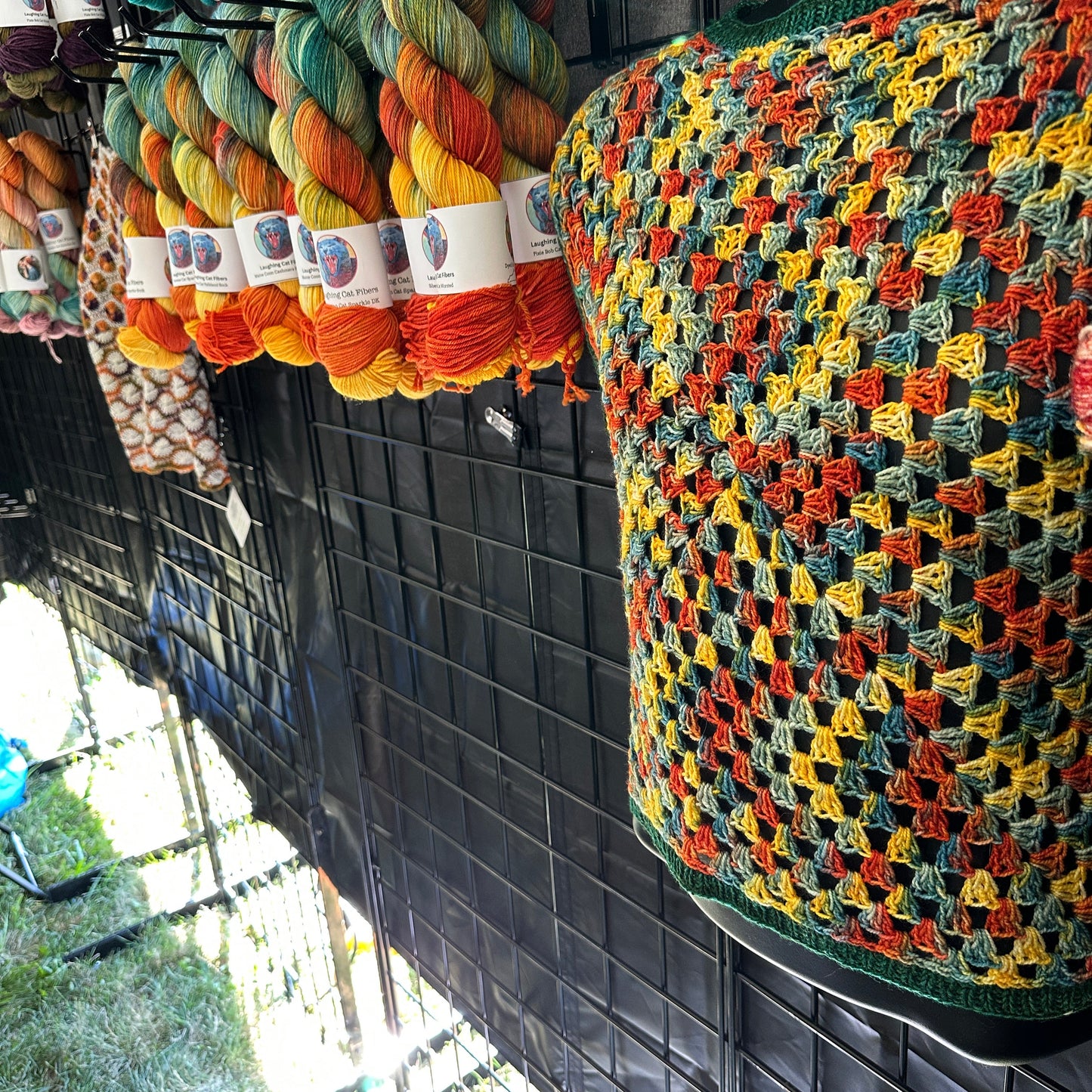 Colorful crocheted garment hanging from a vehicle's sun visor with yarn skeins below.