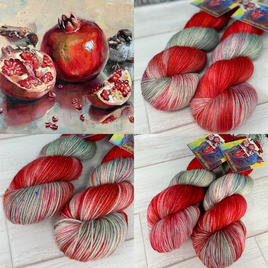 A collection of yarn skeins in shades of red, green, and silver, arranged in a pattern that resembles the composition of a still life painting featuring a pomegranate and a bird.