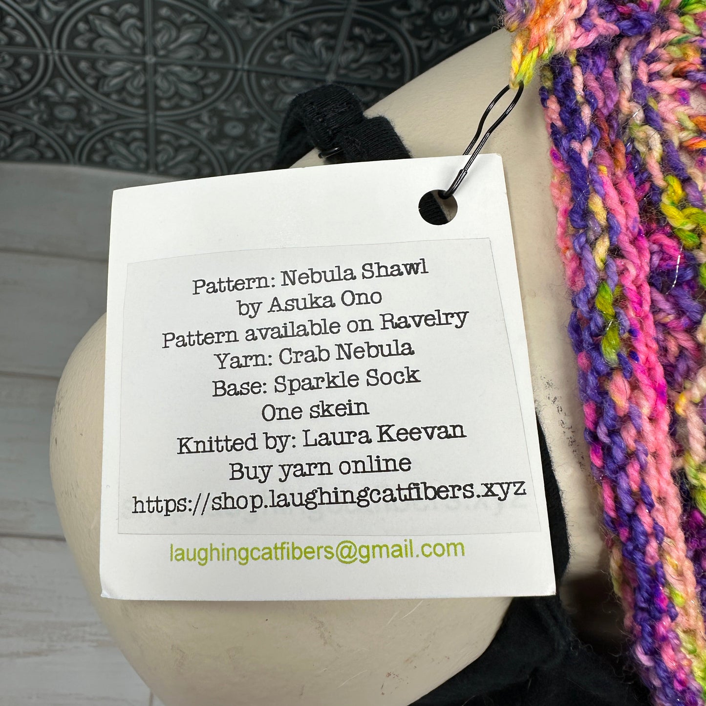Knitted shawl with a label detailing the pattern and yarn information on a mannequin.