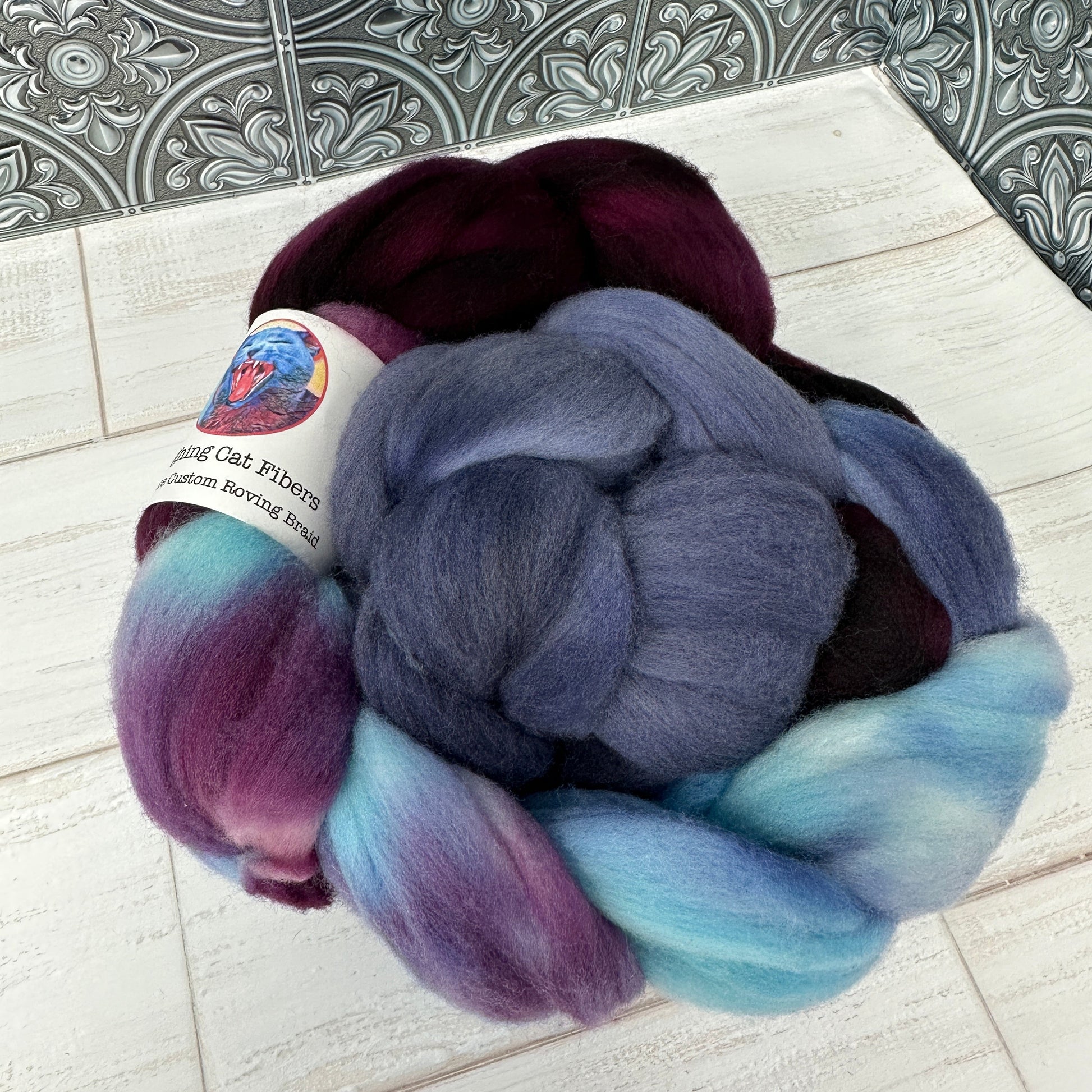 A bundle of purple and blue wool roving dyed in various shades, placed on a surface with a photograph in the background.