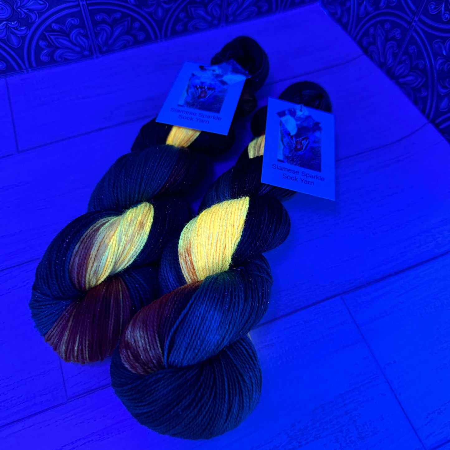 two skeins of hand dyed yarn by Laughing Cat Fibers in their Goldfish colorway under black light 