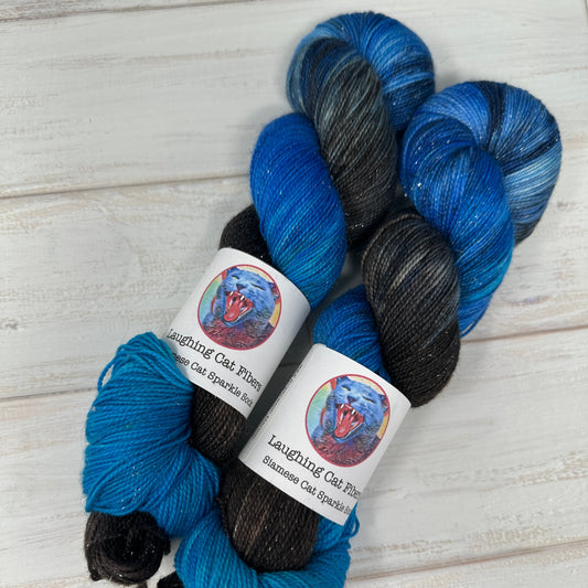 Two skeins of blue and black yarn with labels on a light wooden surface
