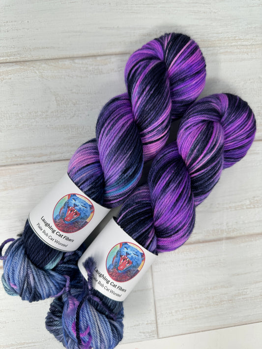Two skeins of purple and blue yarn with labels on a light wooden surface