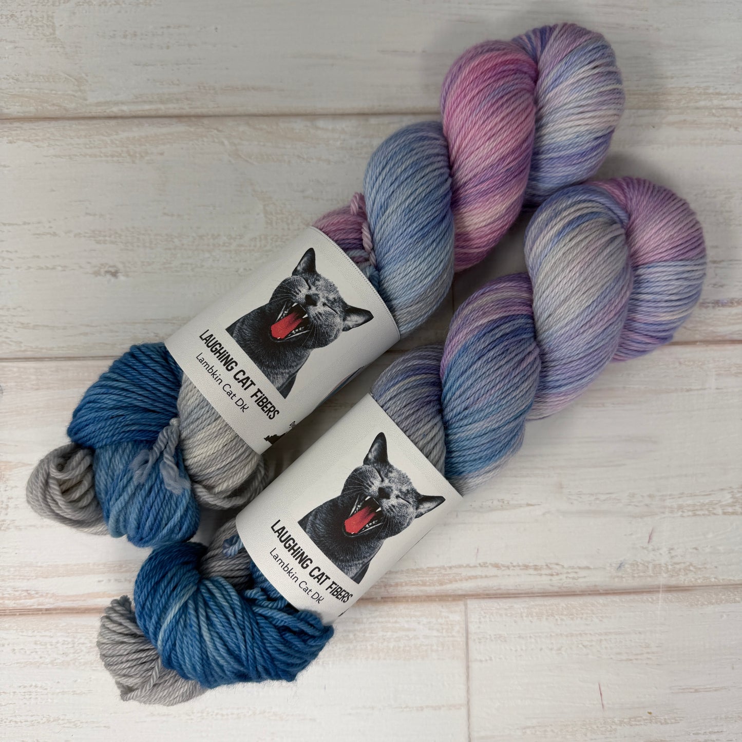 Two skeins of multicolored yarn with 'Laughing Cat Yarns' labels on a wooden surface.