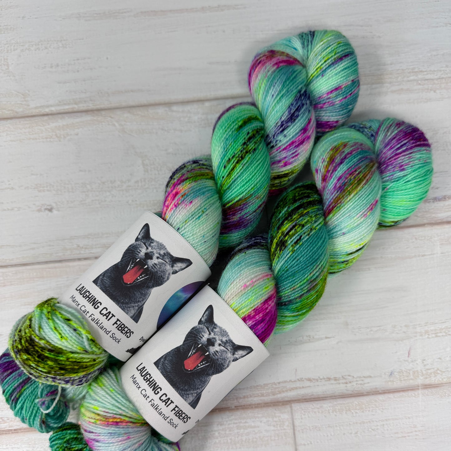 Colorful yarn skeins with 'Laughing Cat Fibres' labels on a wooden surface