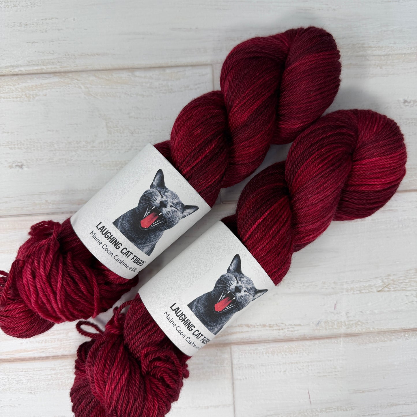 Two skeins of red yarn with labels on a light wooden surface
