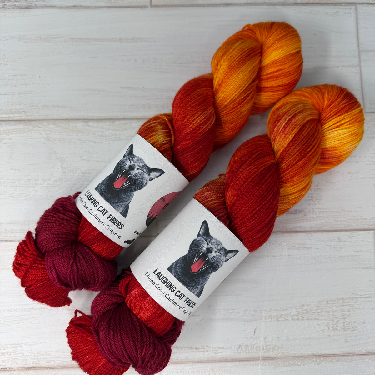 Three skeins of yarn in orange, red, and burgundy on a light wooden surface with labels.