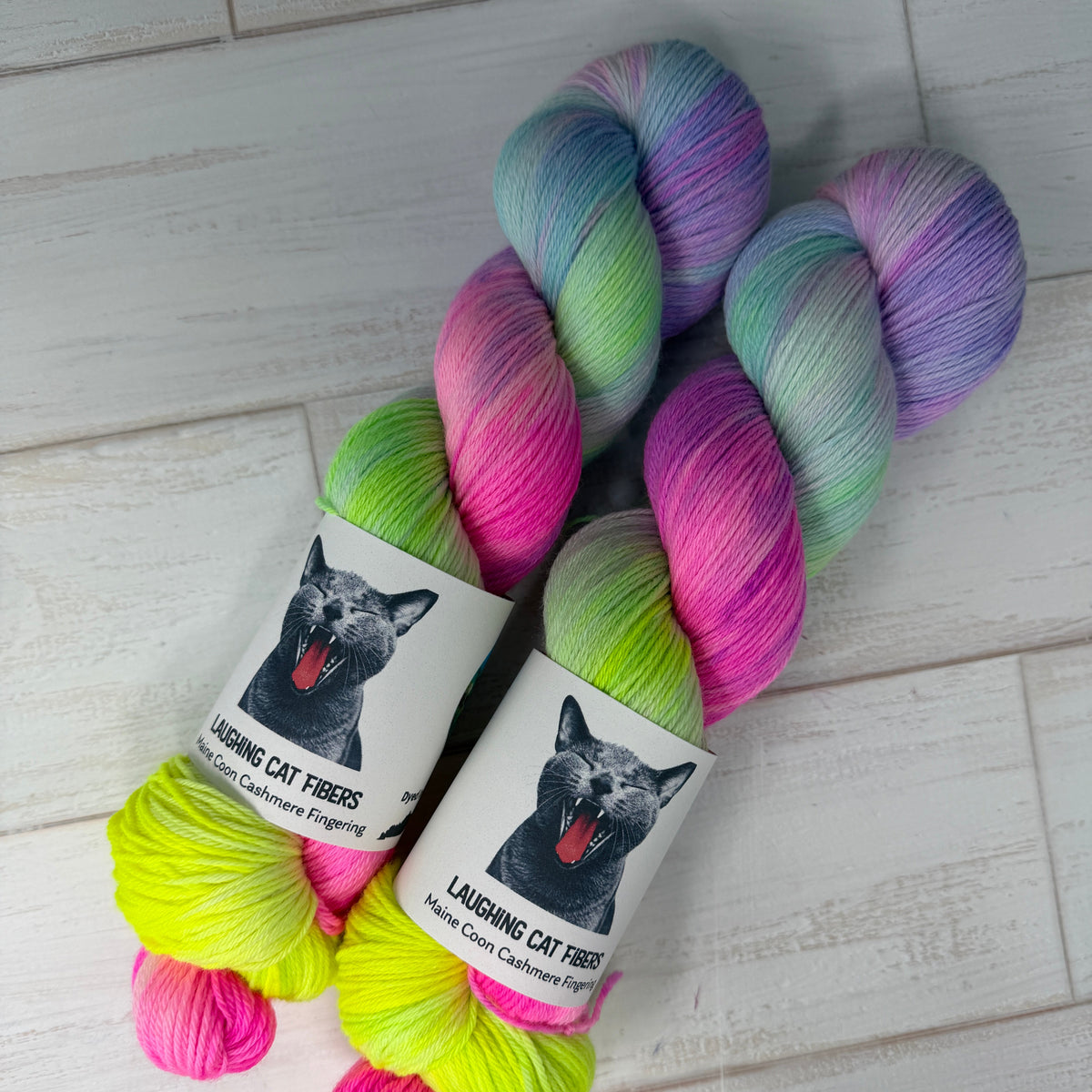 Three skeins of colorful yarn with labels on a light wooden floor.