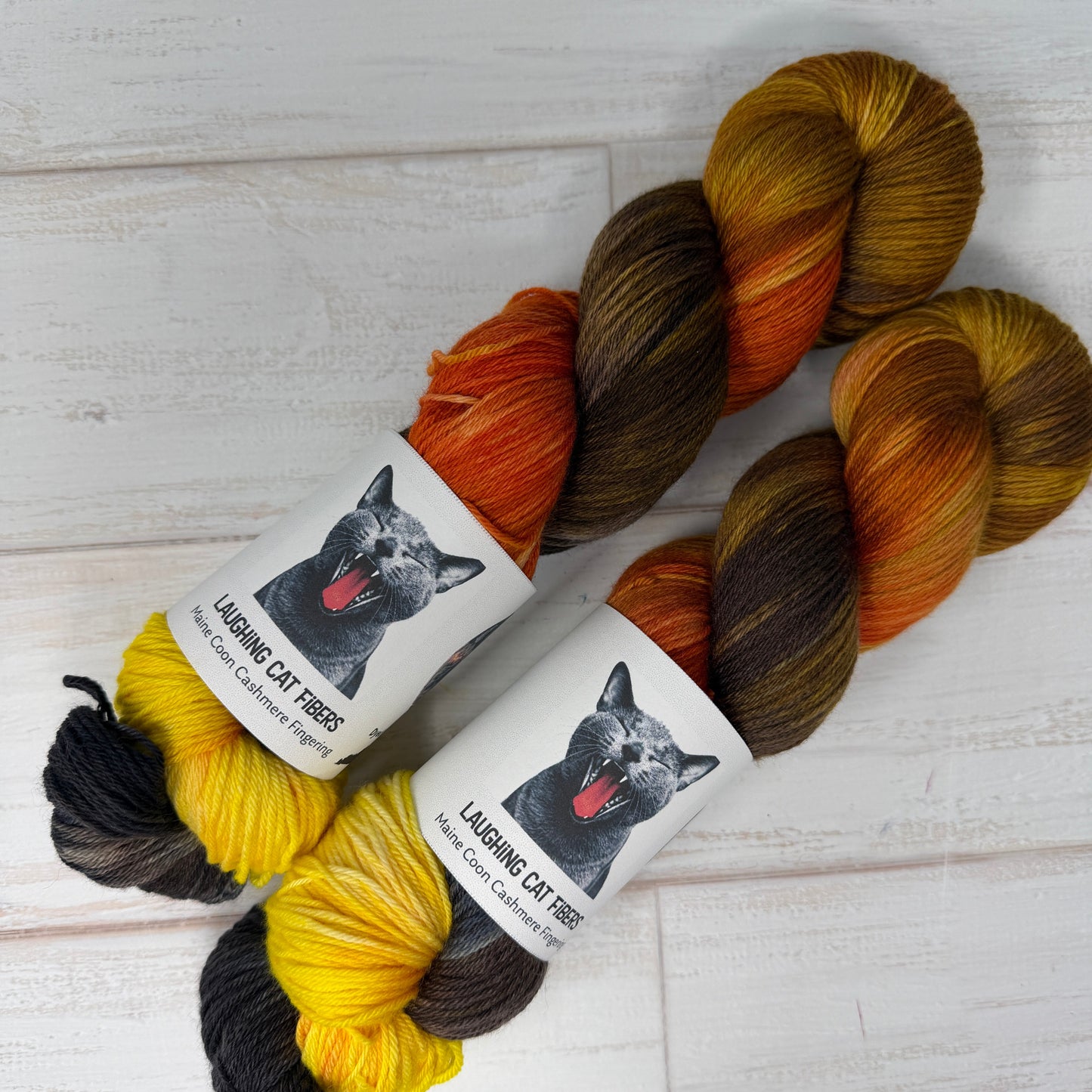 Three skeins of yarn in brown, orange, and yellow with labels on a light wooden surface.