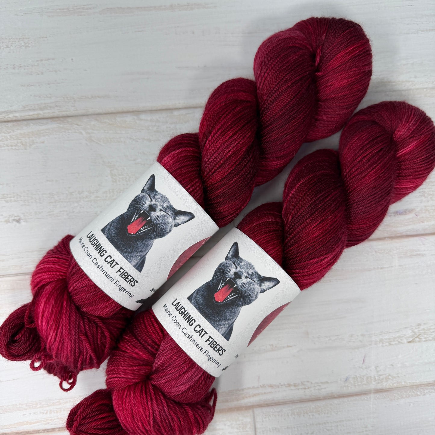 Two skeins of red yarn with labels on a light wooden surface
