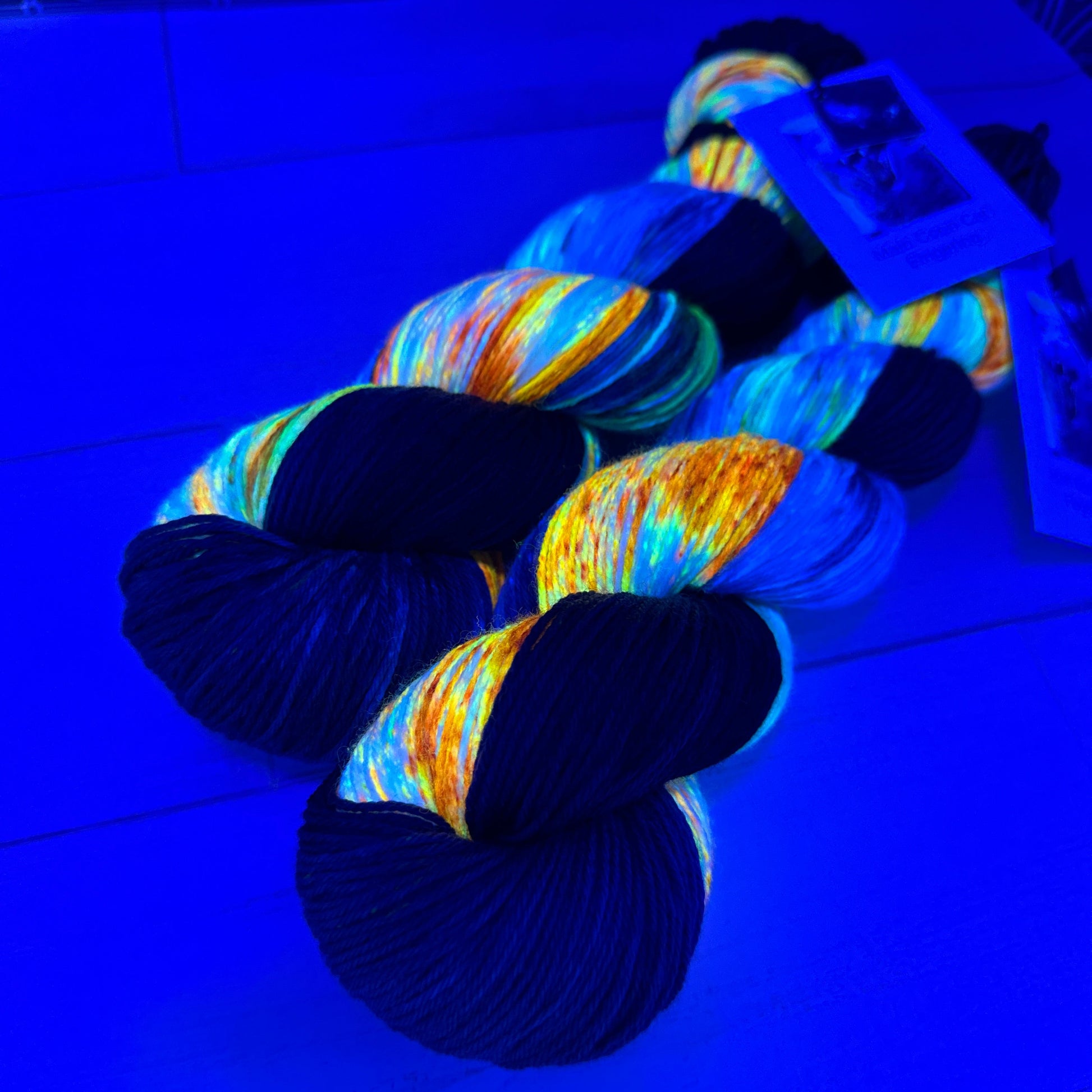 two skeins of hand dyed yarn by Laughing Cat Fibers under black light Hand of God colorway 