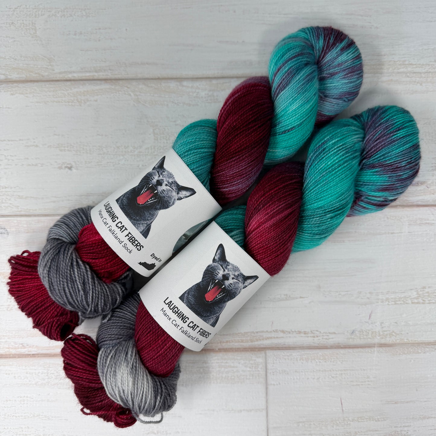 Three skeins of yarn in teal, red, and gray with labels on a light wooden surface.