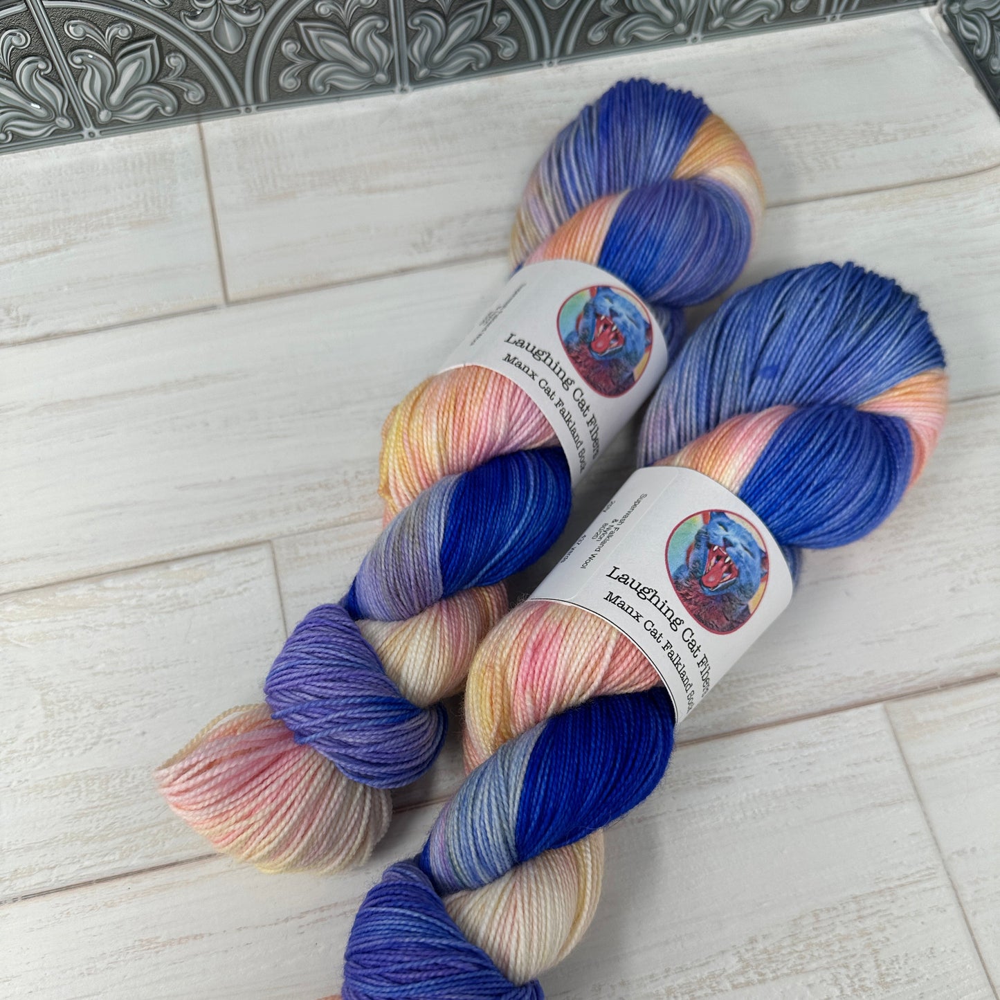 Two skeins of multicolored yarn with labels on a light wooden surface.