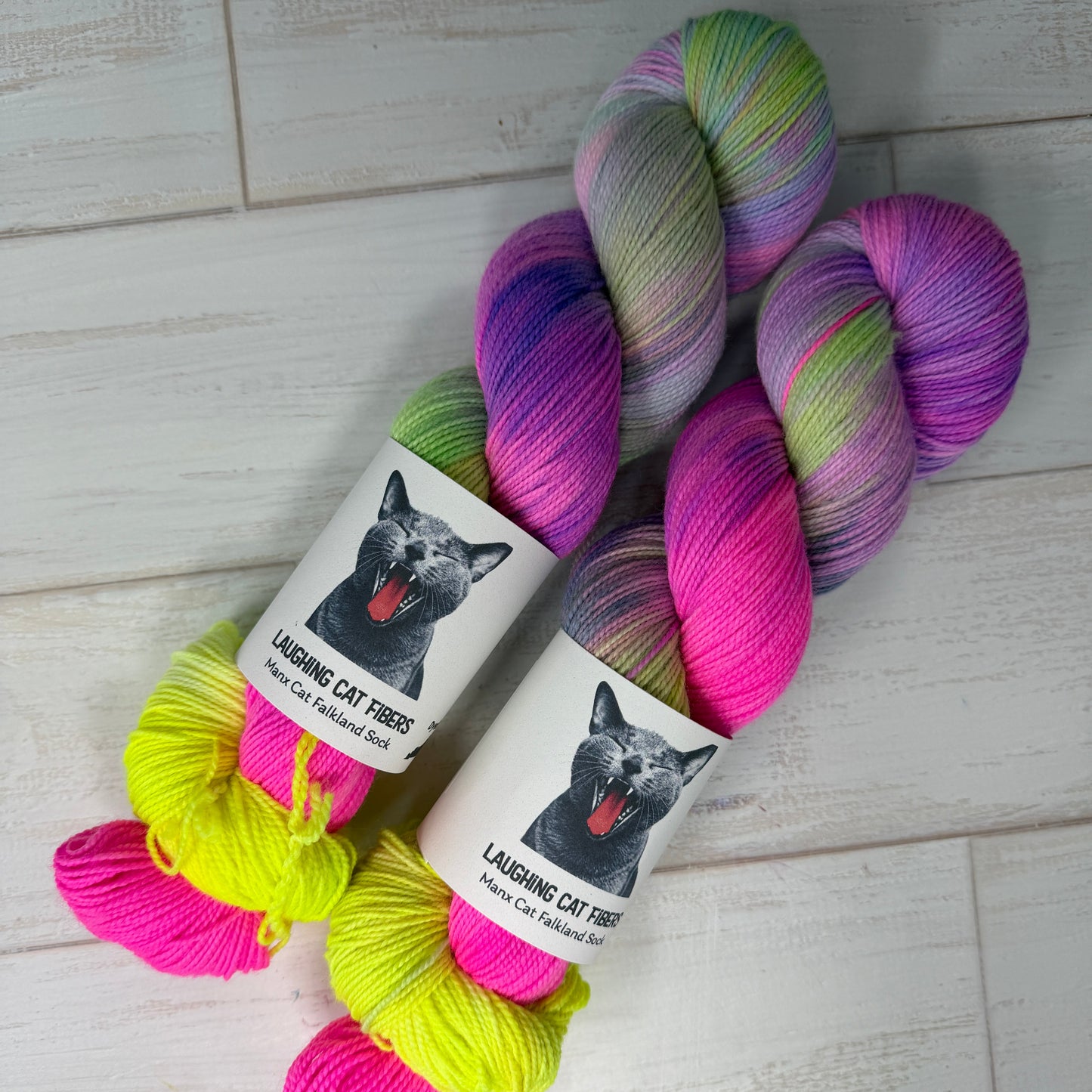 Colorful yarn skeins with a cat-themed label on a light wooden floor.
