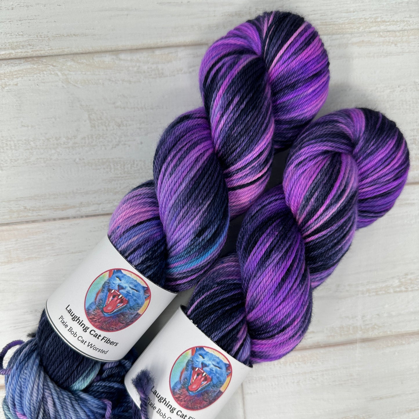 Two skeins of purple and blue yarn with labels on a light wooden surface
