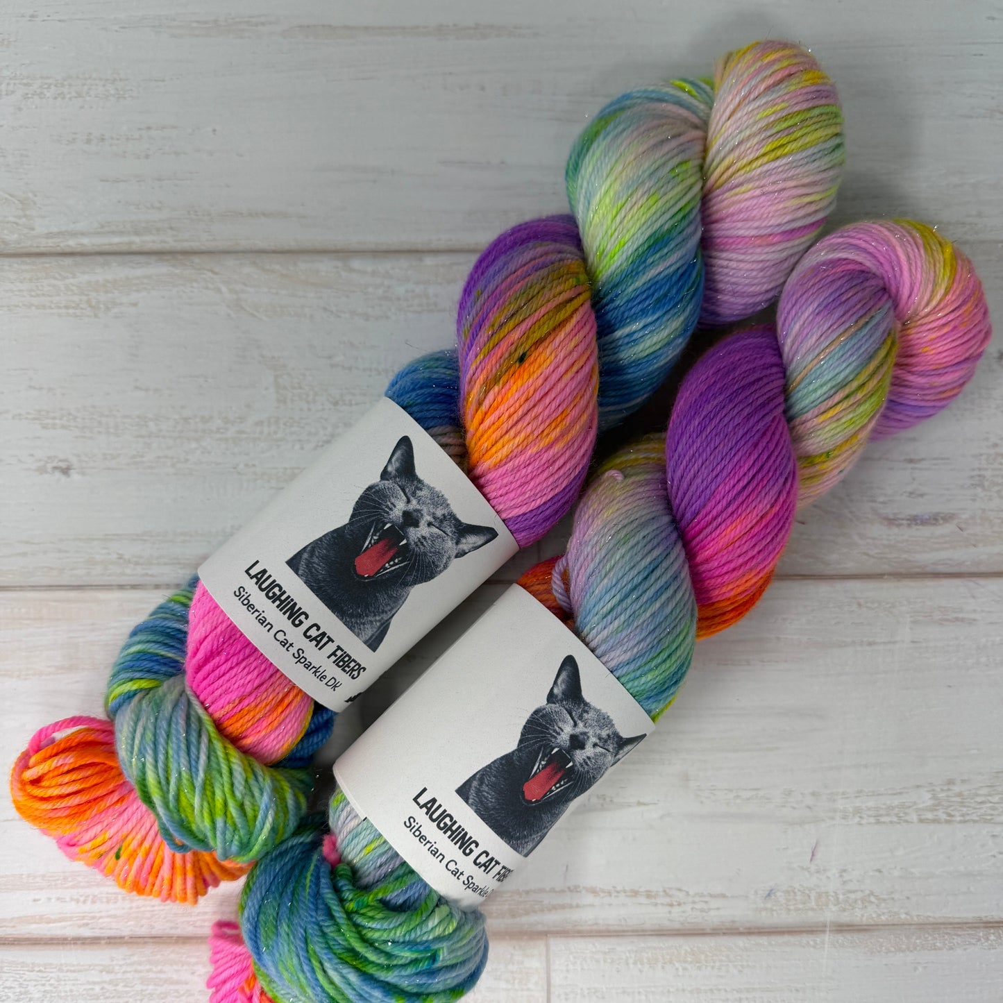 Colorful skein of yarn with a 'Laughing Cat Fibres' label on a wooden surface