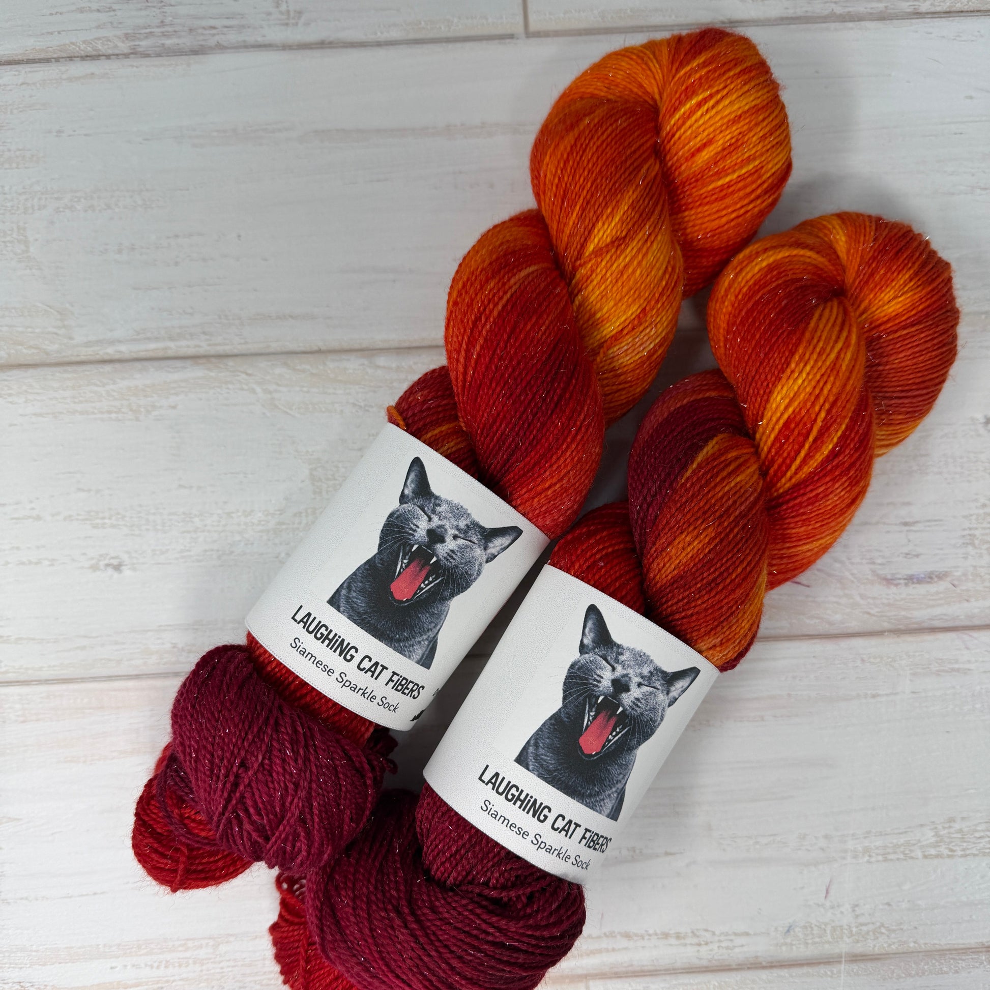 Three skeins of red and orange yarn with labels on a light wooden surface