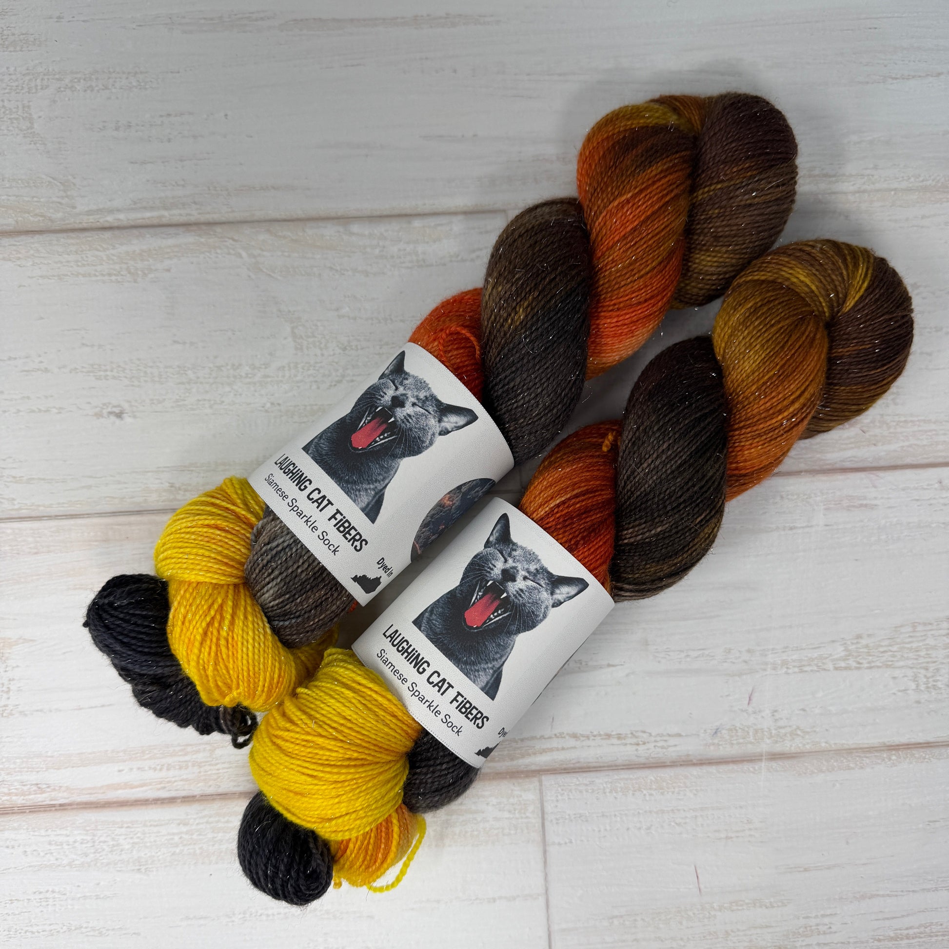 Three skeins of yarn in brown, orange, and yellow with a label on a light wooden surface.