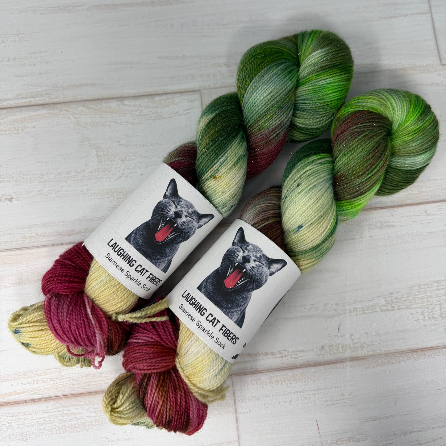 Two skeins of yarn with gradient colors and 'Lazing Cat Yarns' labels on a wooden surface.