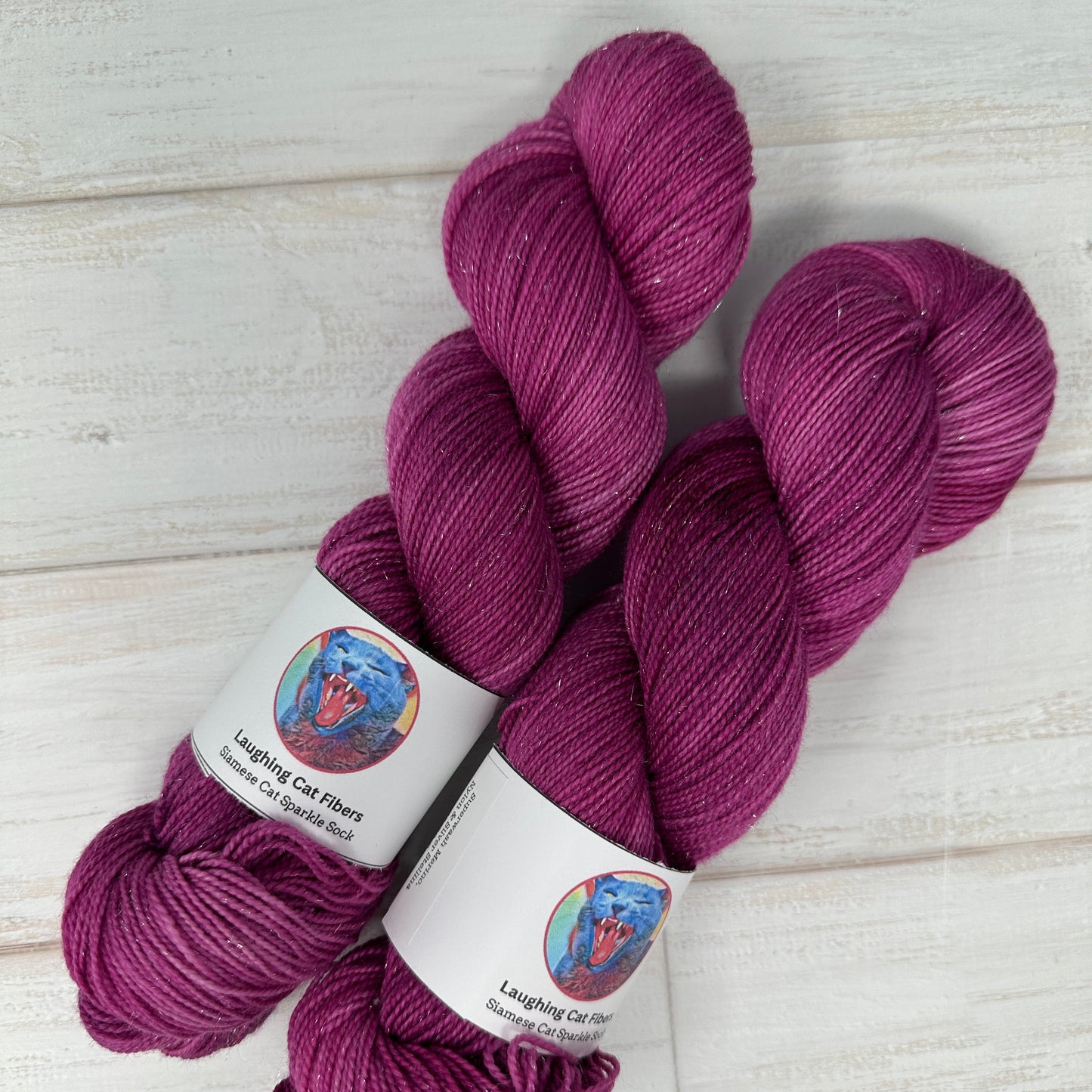 Three skeins of purple yarn with labels on a light wooden surface
