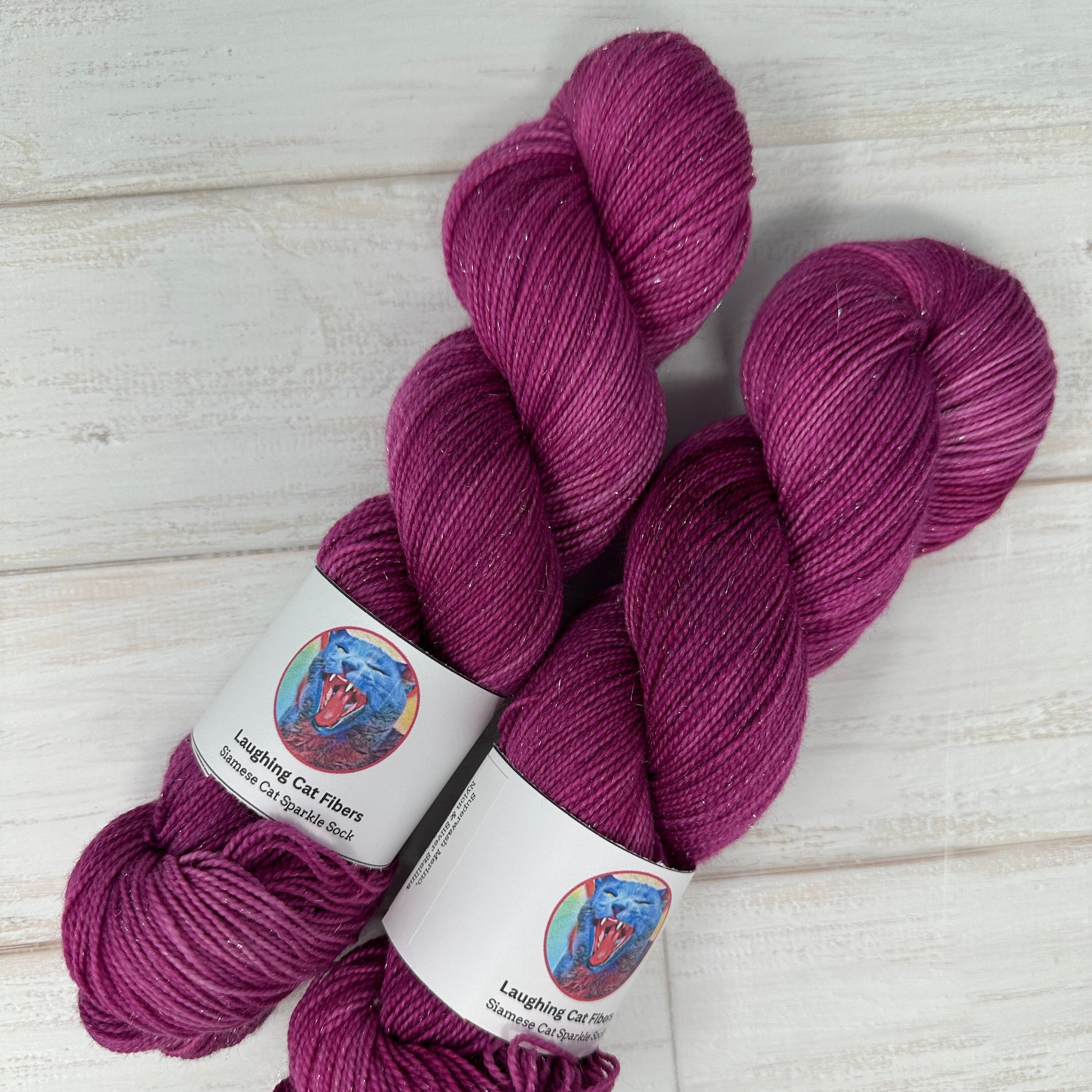Three skeins of purple yarn with labels on a light wooden surface