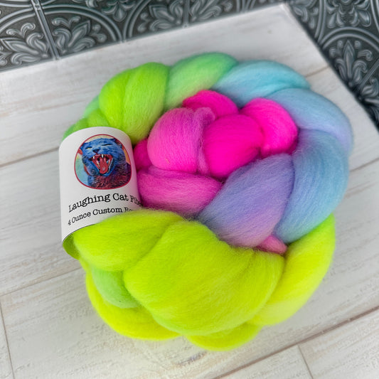 A bundle of colorful wool roving dyed in shades of pink, blue, green, and yellow, placed on a white surface with a patterned backdrop.