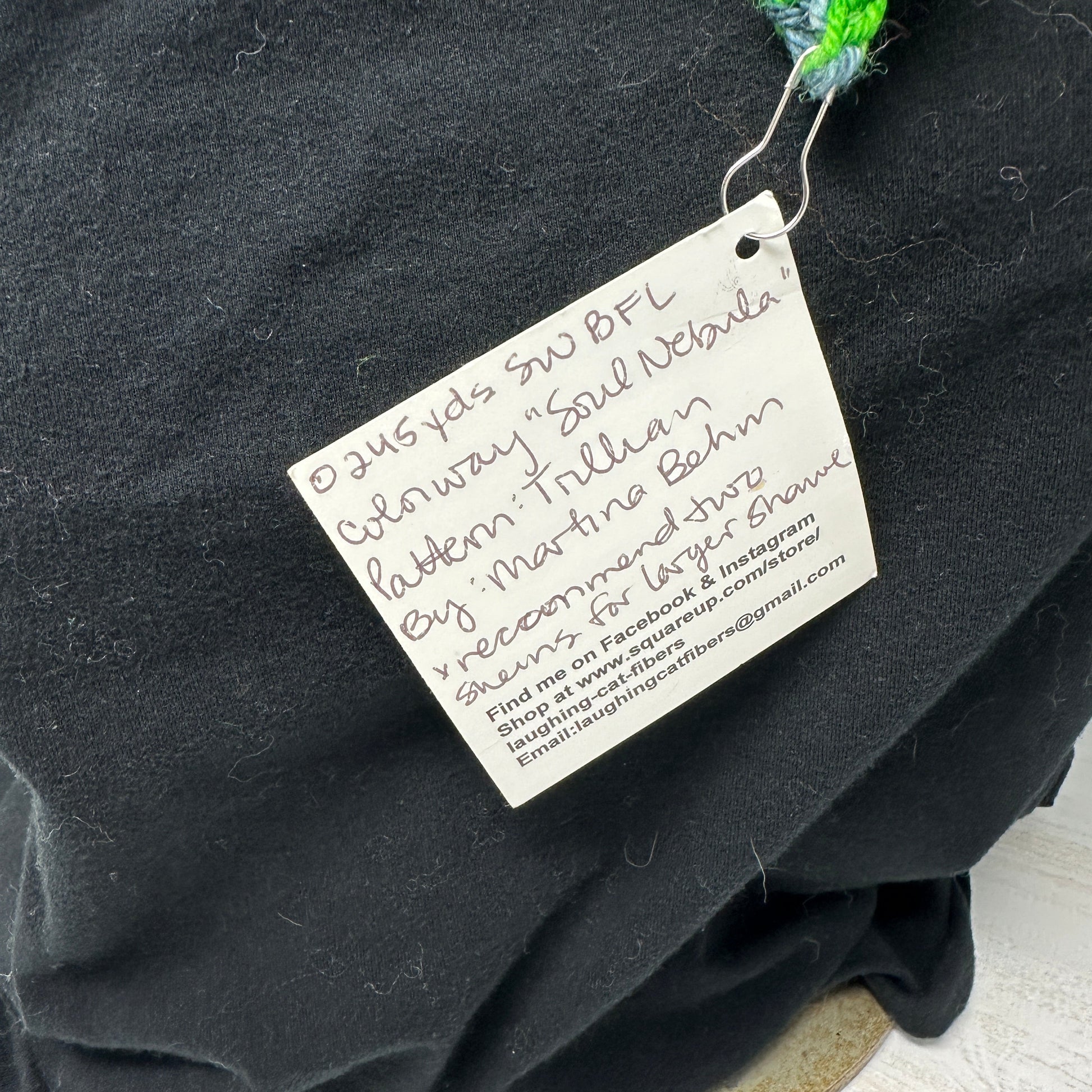 Black fabric with a label and green textured object on a light wooden surface