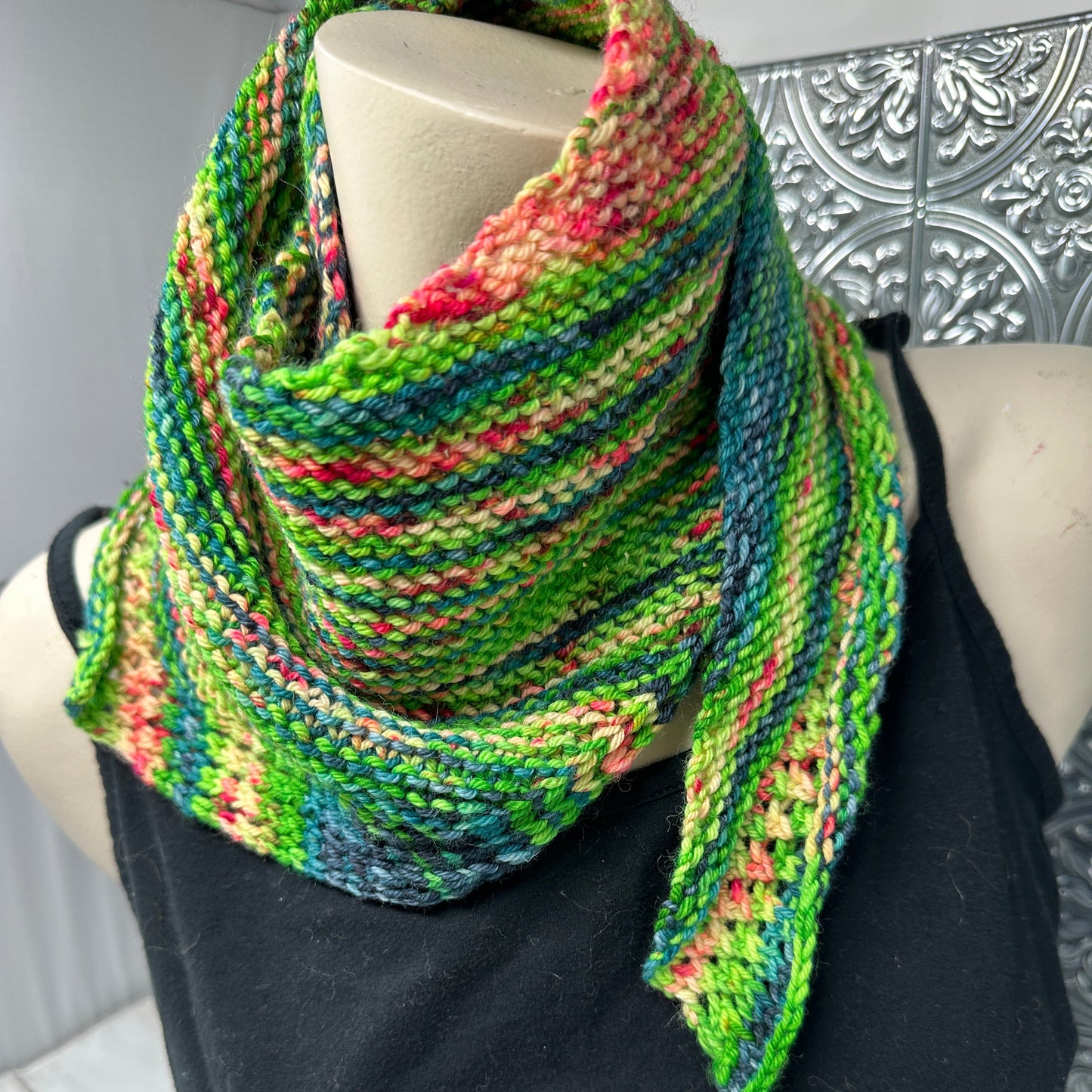 Colorful knitted scarf on a mannequin with a decorative wall in the background
