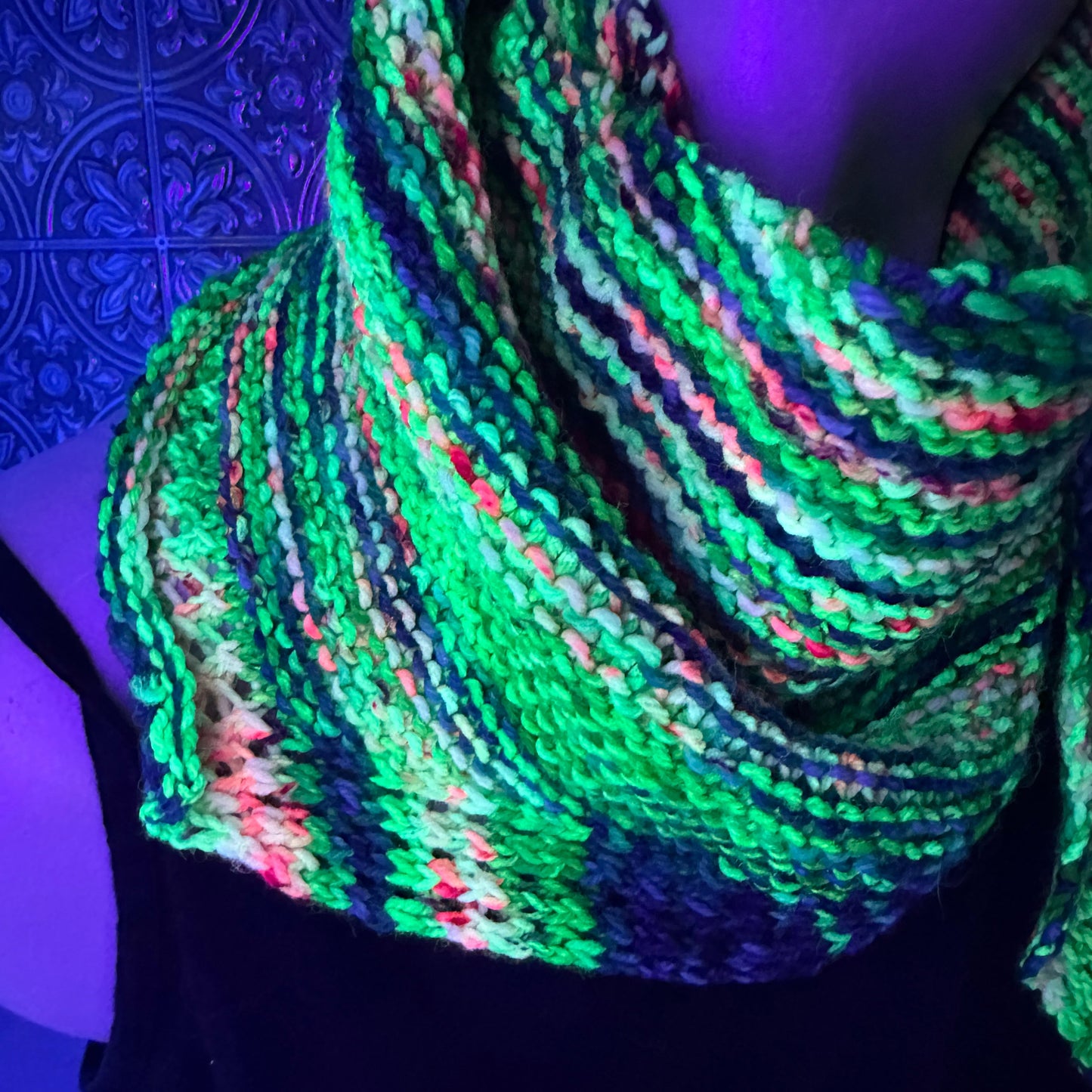 Colorful knitted scarf on a mannequin against a patterned wall.