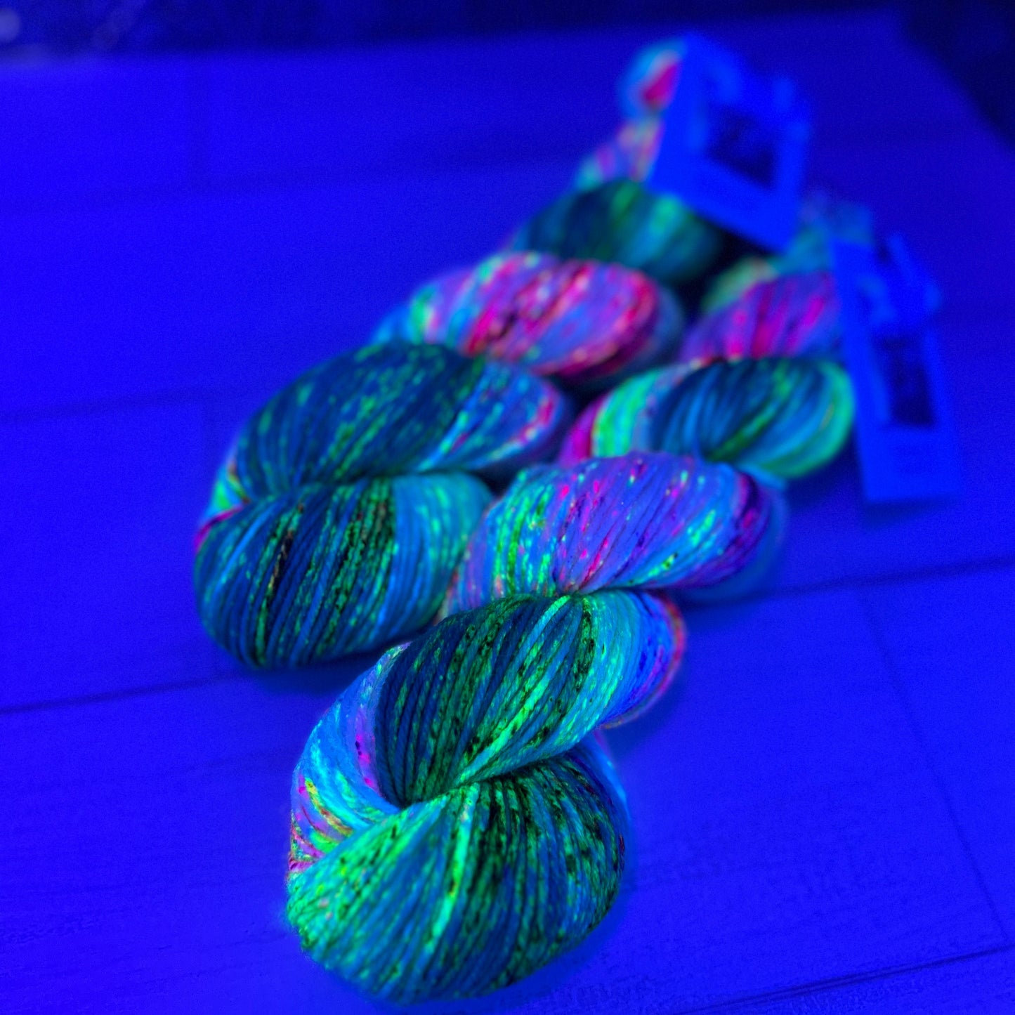two skeins of multicolored yarn under black light by Laughing Cat Fibers