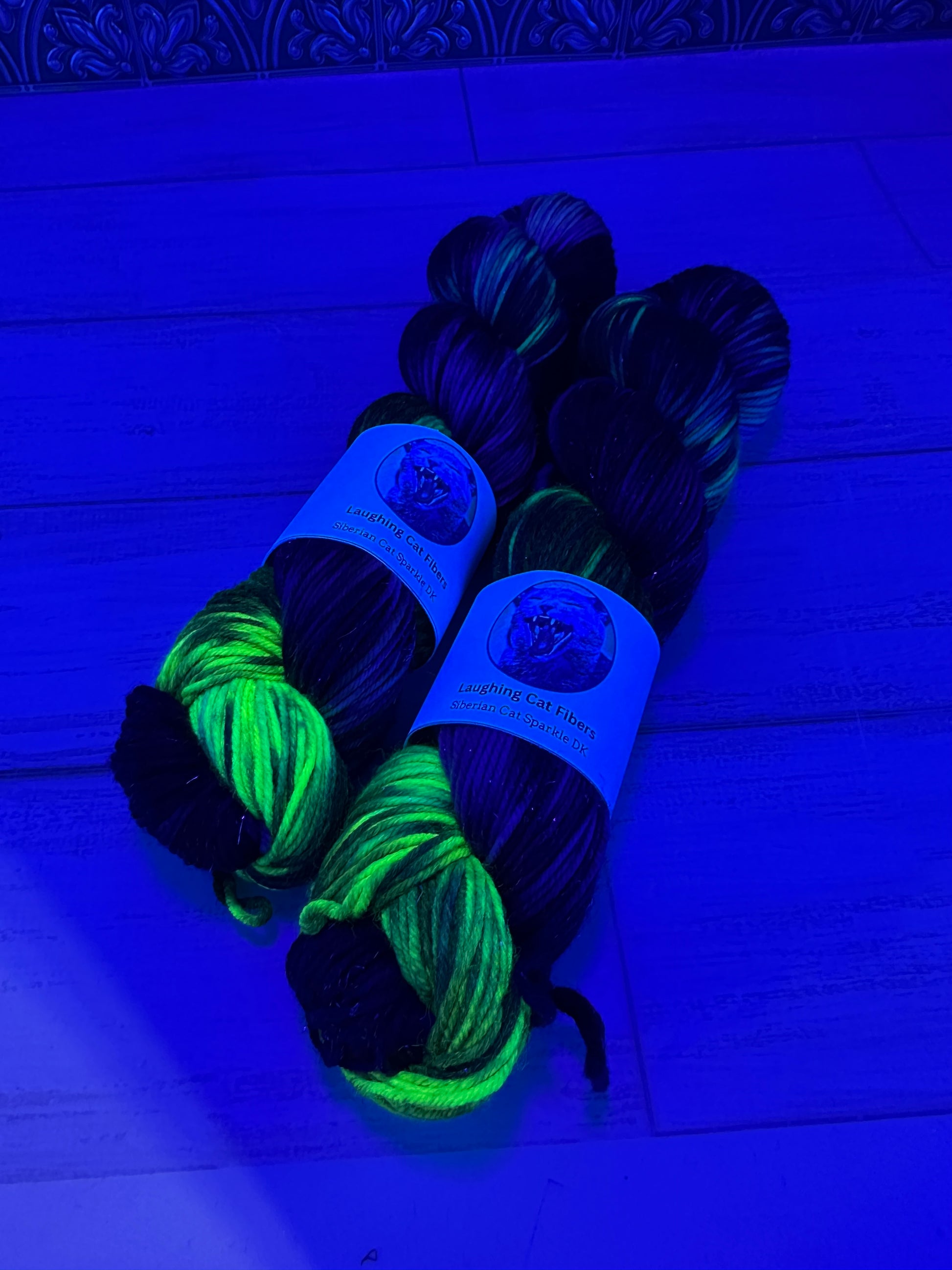 Two skeins of yarn, one black and one green, under a black light on a wooden surface.