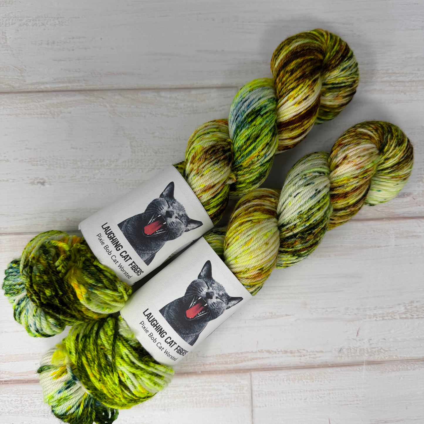 Two skeins oF black light yarn with 'Laughing Cat Yarns' labels on a light wooden surface.