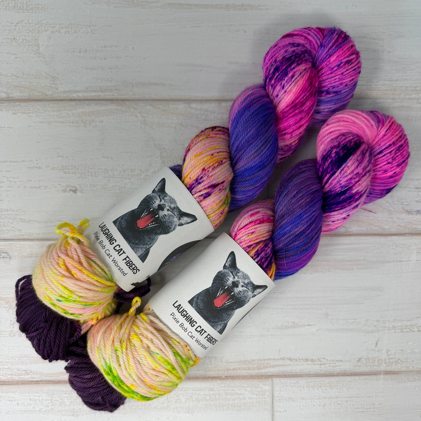 Colorful yarn skeins with 'Laughing Cat Fibres' labels on a light wooden surface