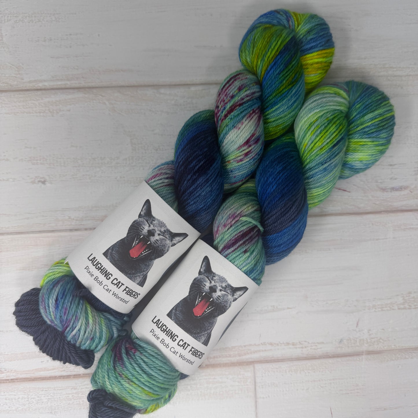 Multicolored yarn skeins with 'Laughing Cat Fibres' labels on a wooden surface