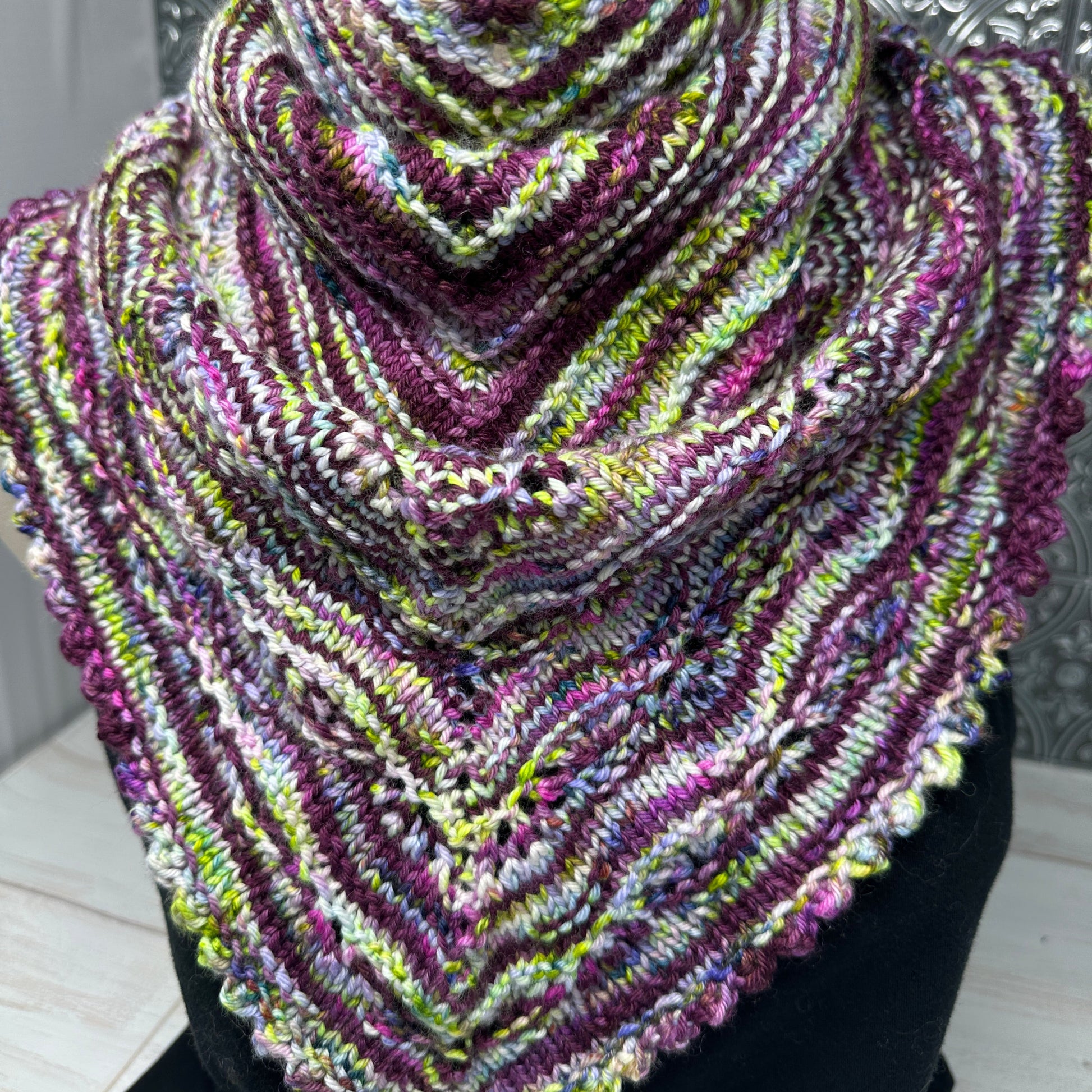 Multicolored knitted scarf on a mannequin against a decorative wall.