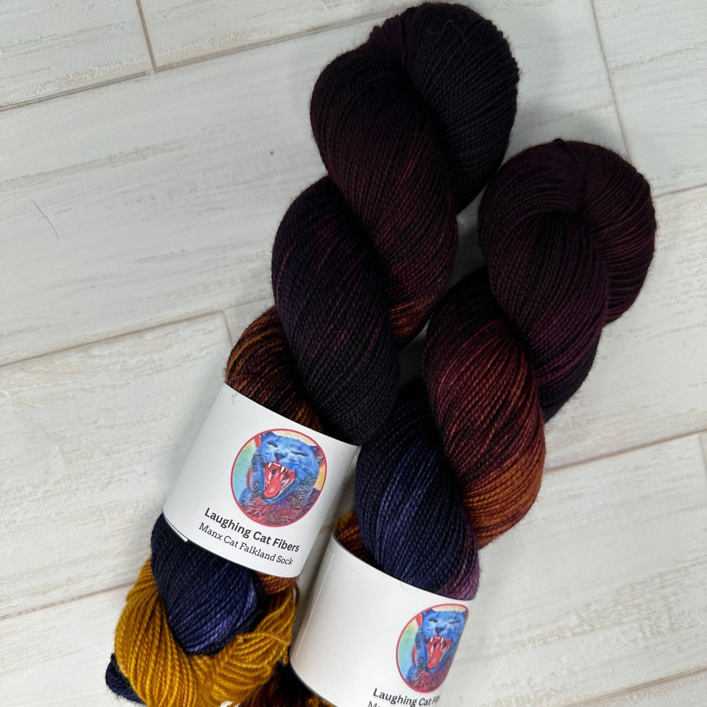 Two skeins of yarn in dark brown, blue, and gold on a light wooden surface.