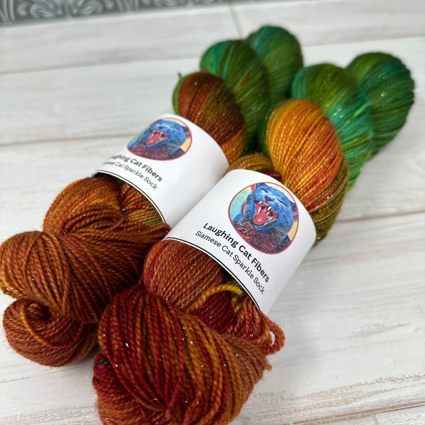 Three skeins of yarn in green, orange, and brown with labels on a light wooden surface.