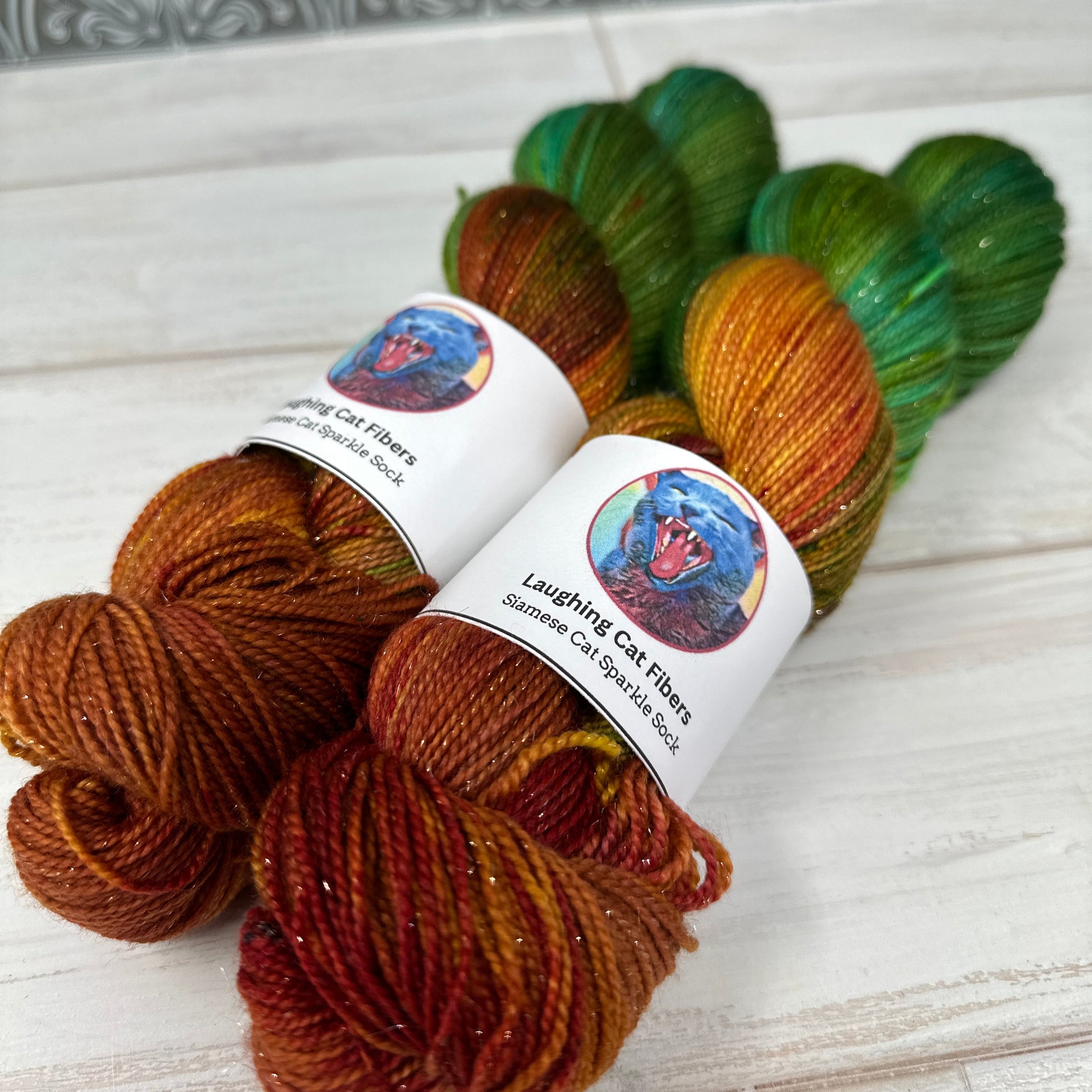 Three skeins of yarn in green, orange, and brown with labels on a light wooden surface.