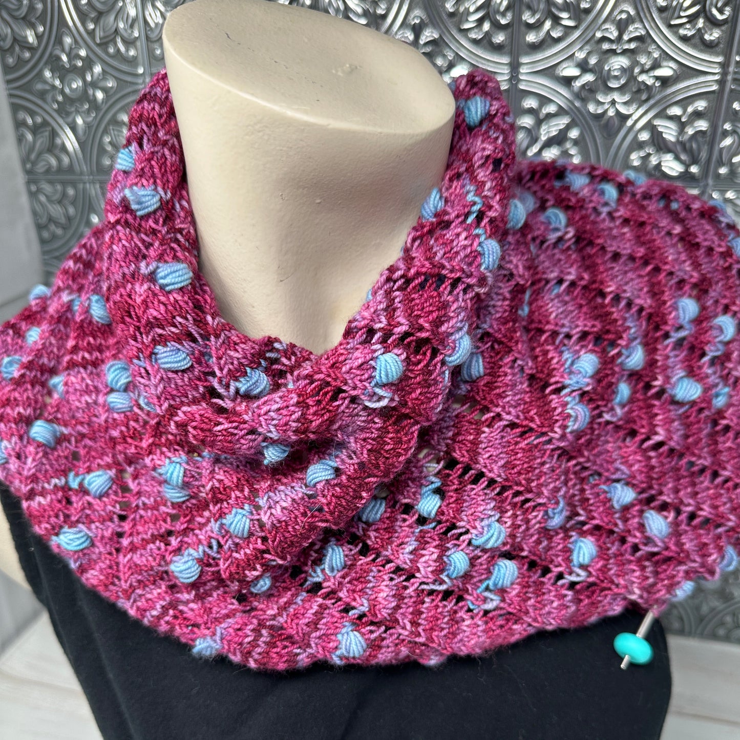 Pink knitted scarf with blue accents on a mannequin held by a person wearing black gloves.