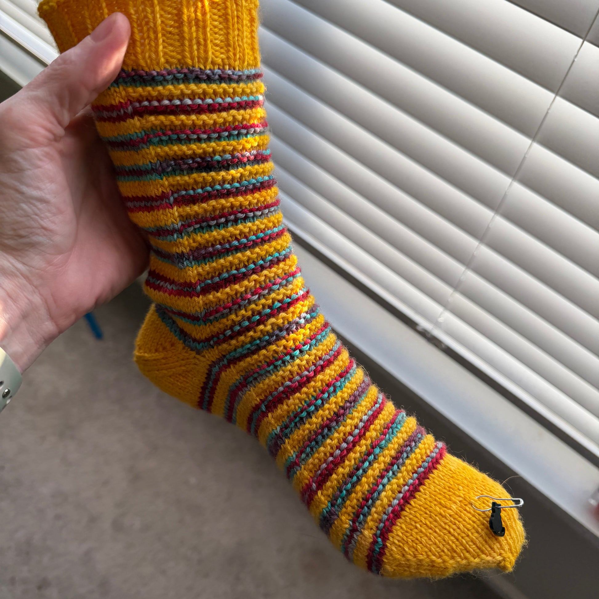 Hand holding a colorful striped sock against a neutral background