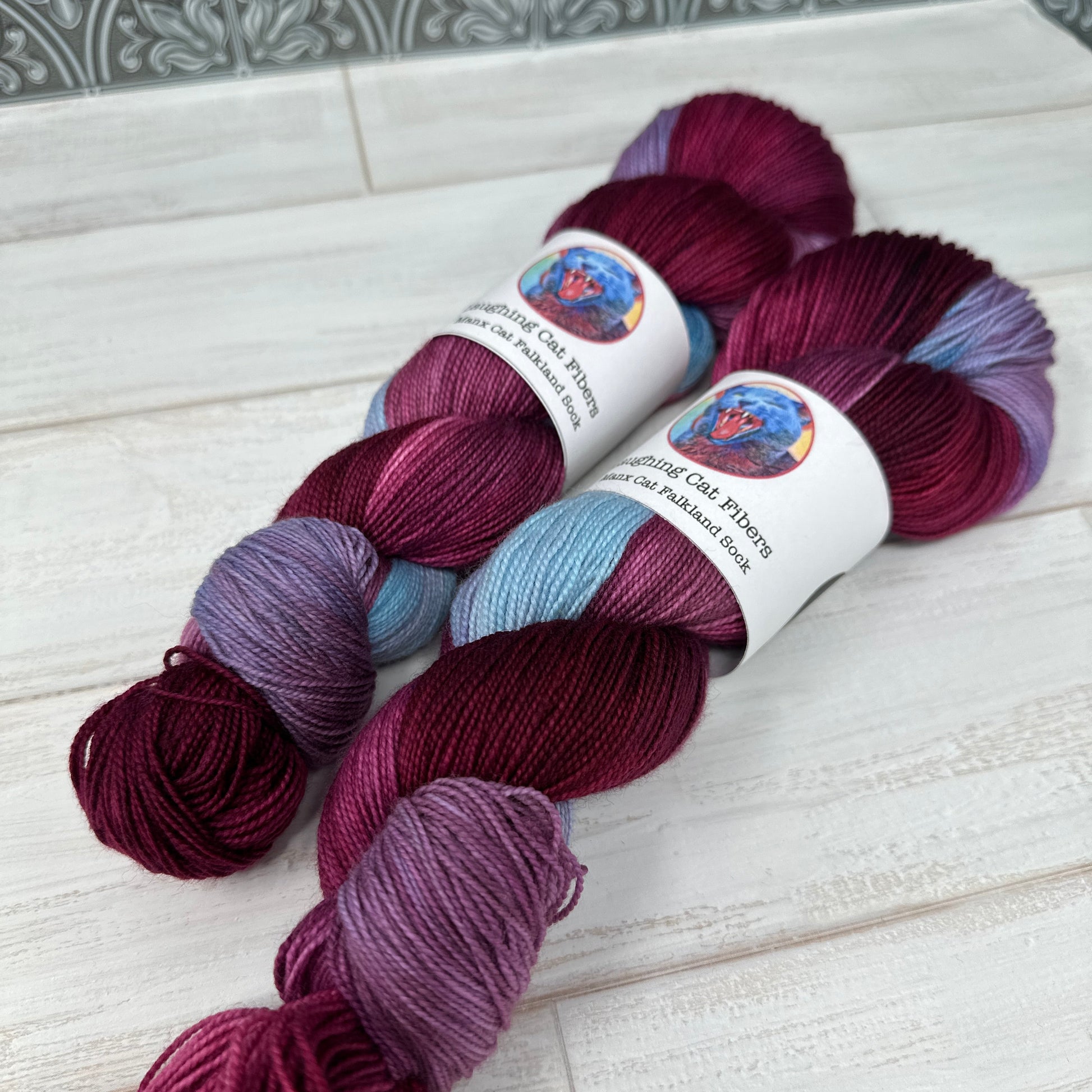 Three skeins of multicolored yarn on a white surface with a patterned tile background.