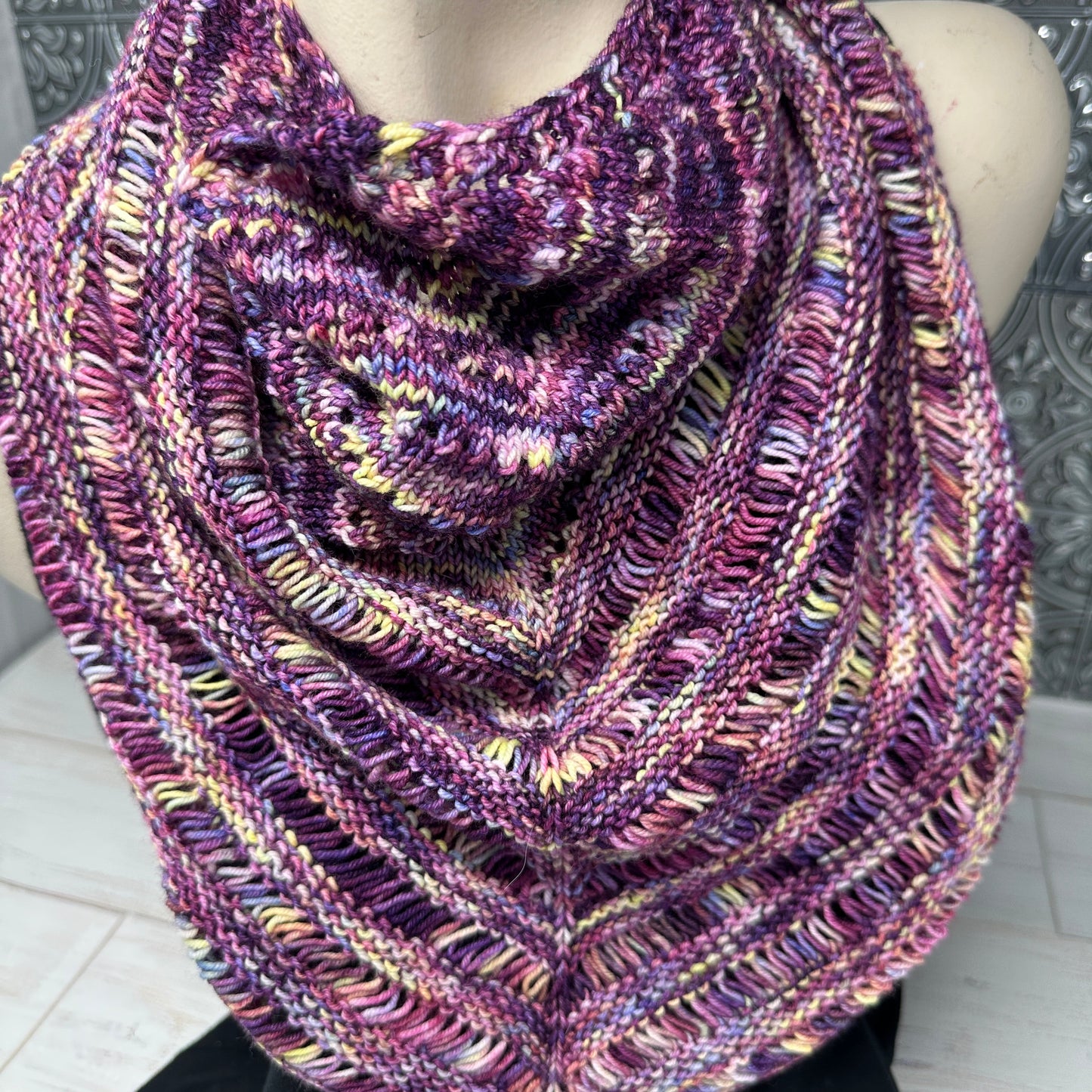 Multicolored knitted scarf on a mannequin against a patterned wall.