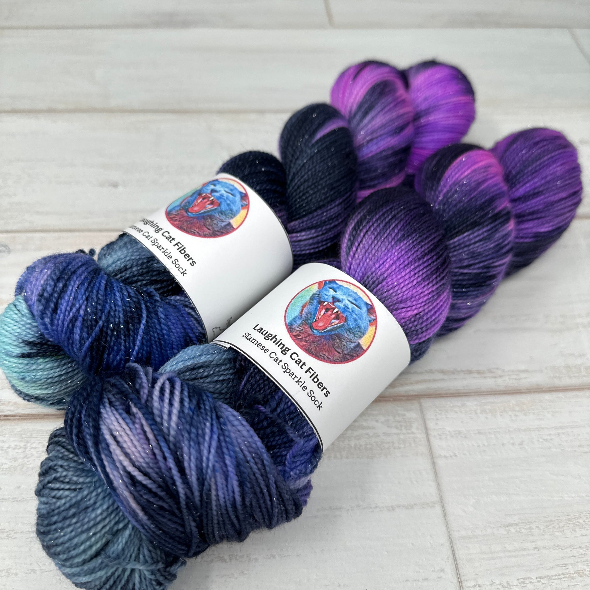 Two skeins of yarn in purple, blue, and green on a light wooden surface with a decorative border.