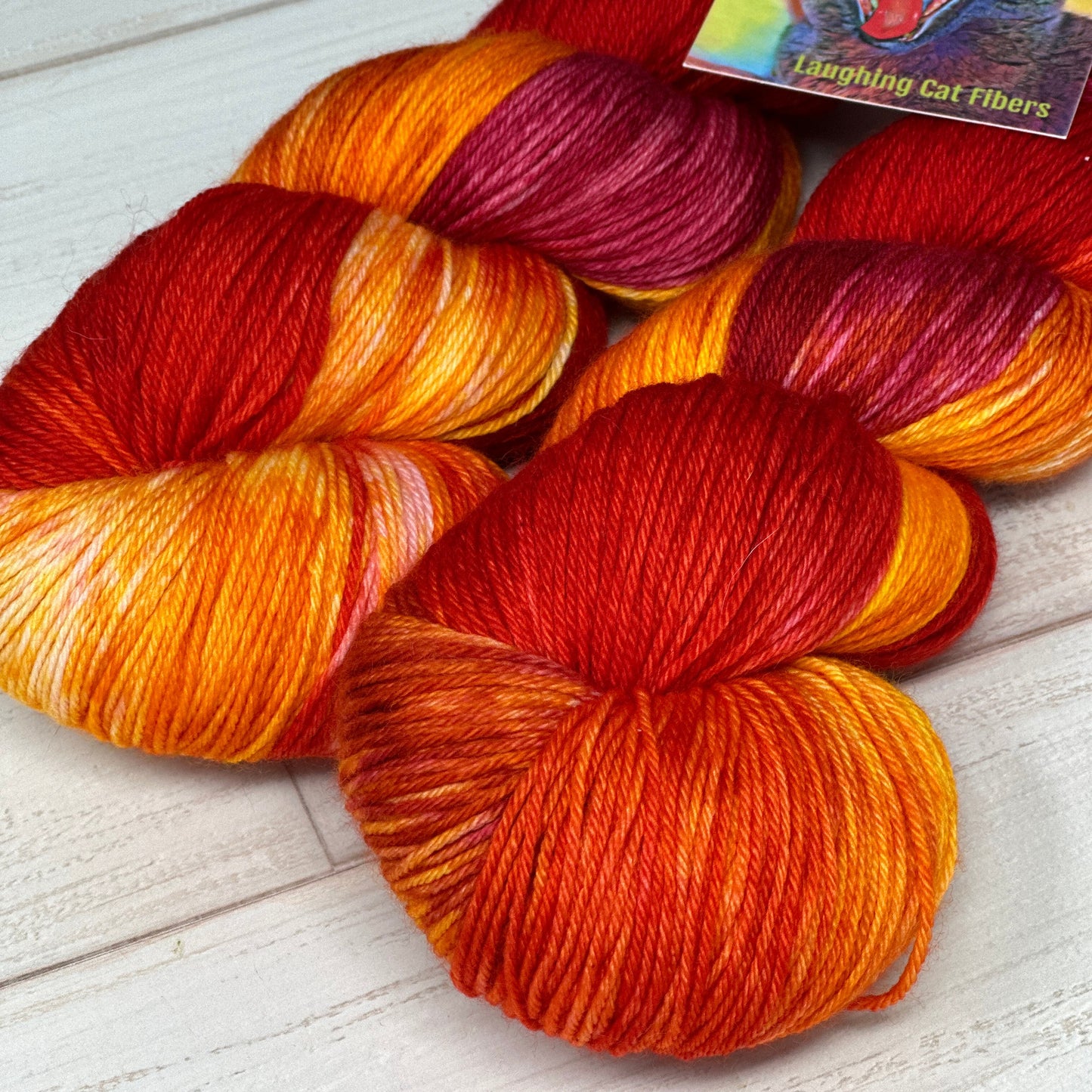 Three skeins of orange and red merino cashmere and nylon yarn dyed by Laughing Cat Fibers in her 1984 colorway 