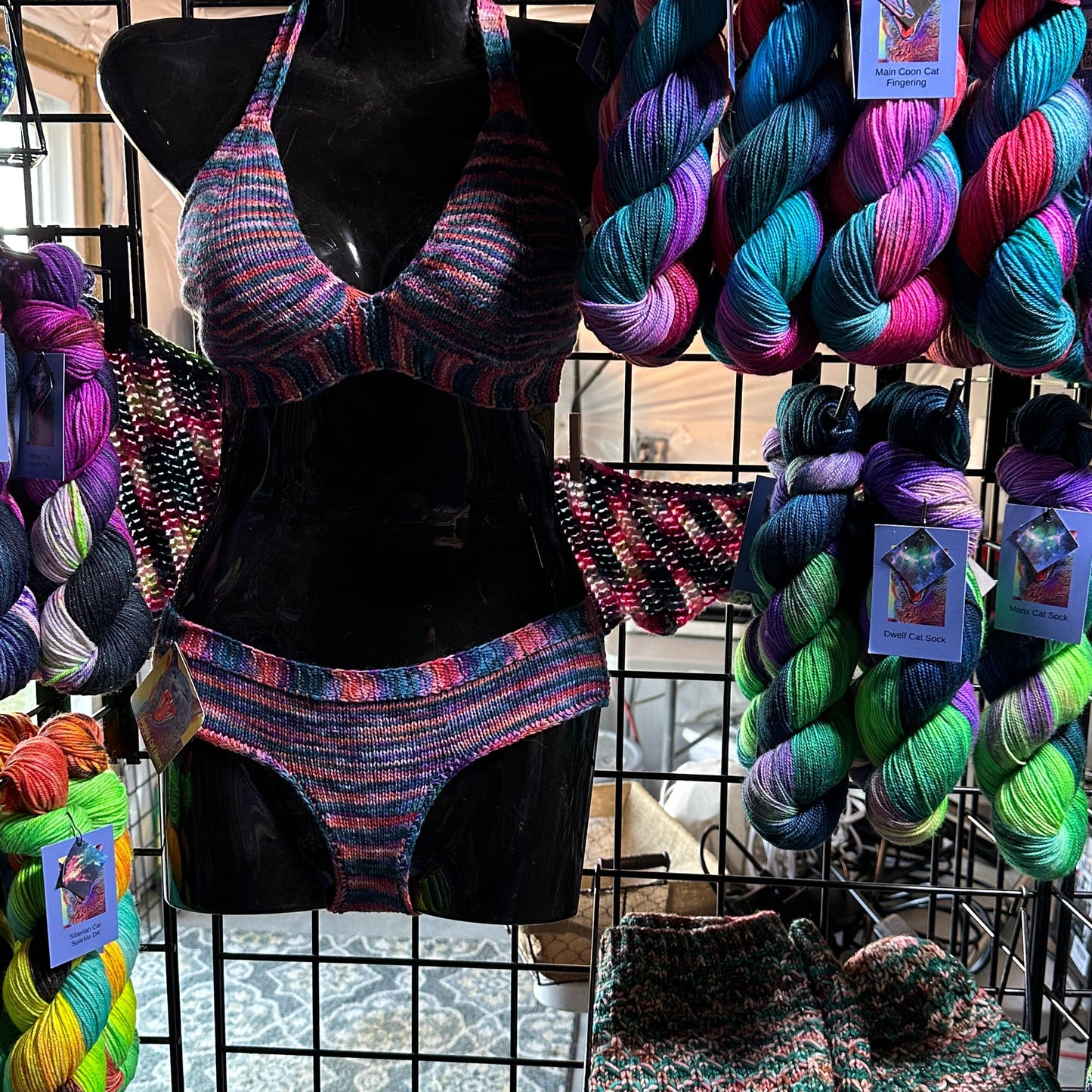 Colorful yarn skeins and knitted items displayed on a wire rack.