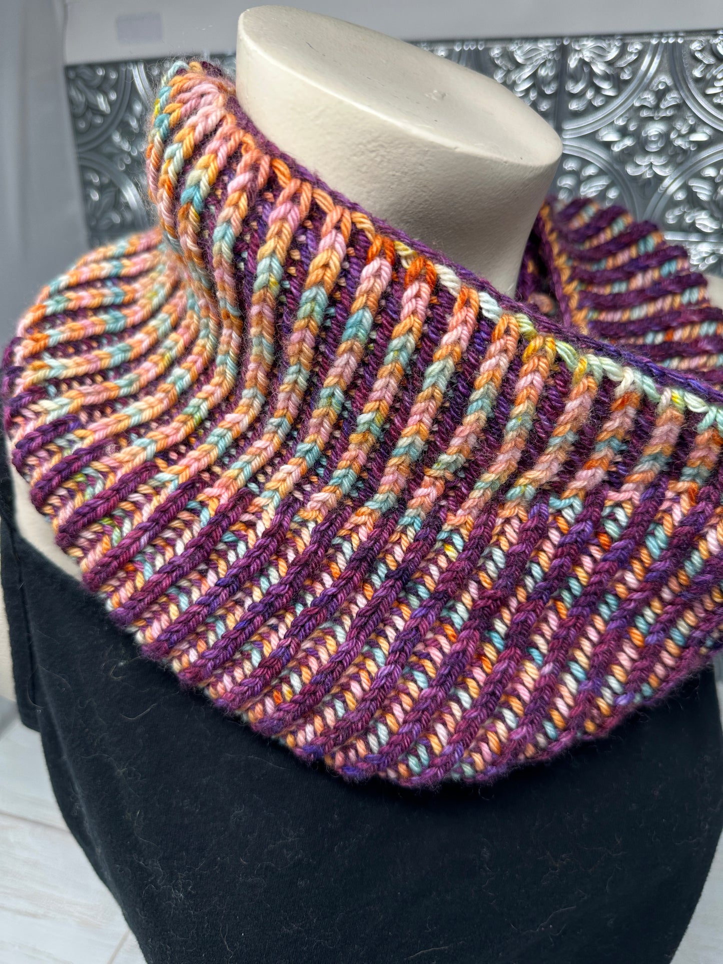 Multicolored knitted scarf on a black surface with a decorative wall in the background