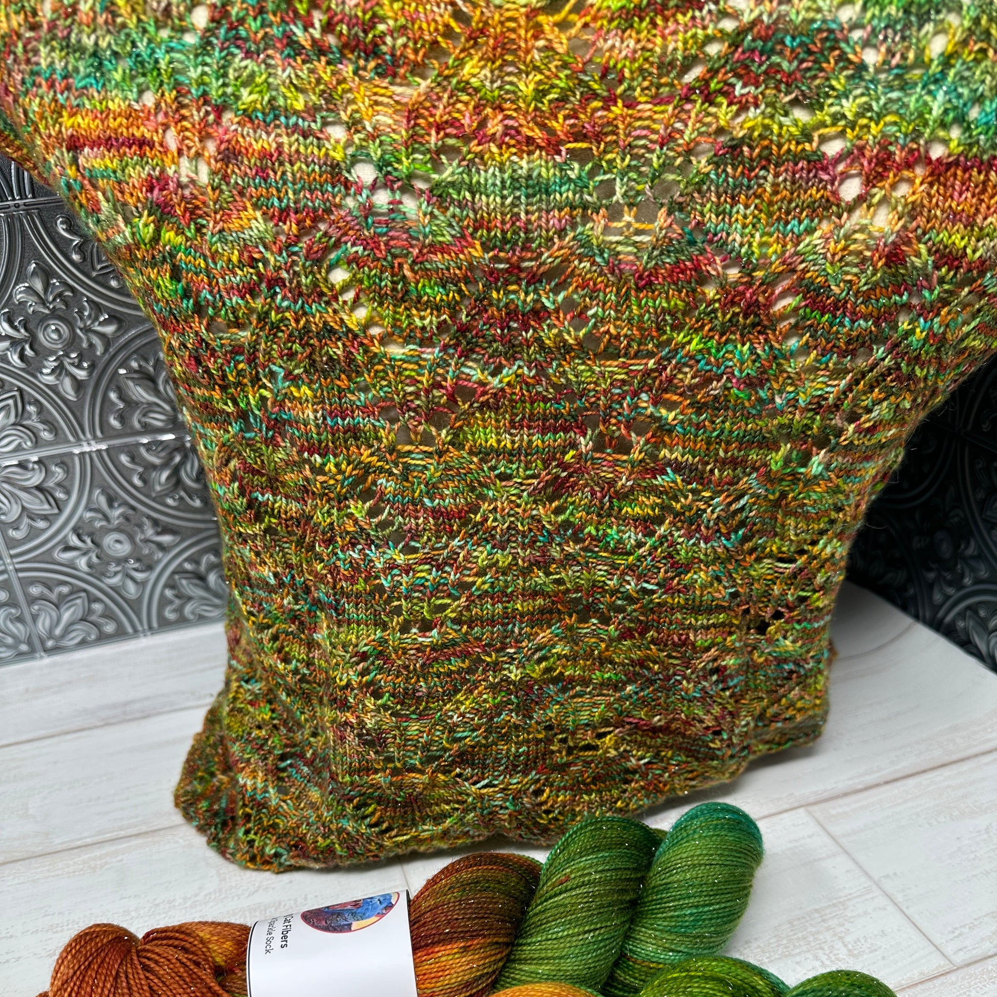 Colorful knitted sock and skeins of yarn on a tiled floor