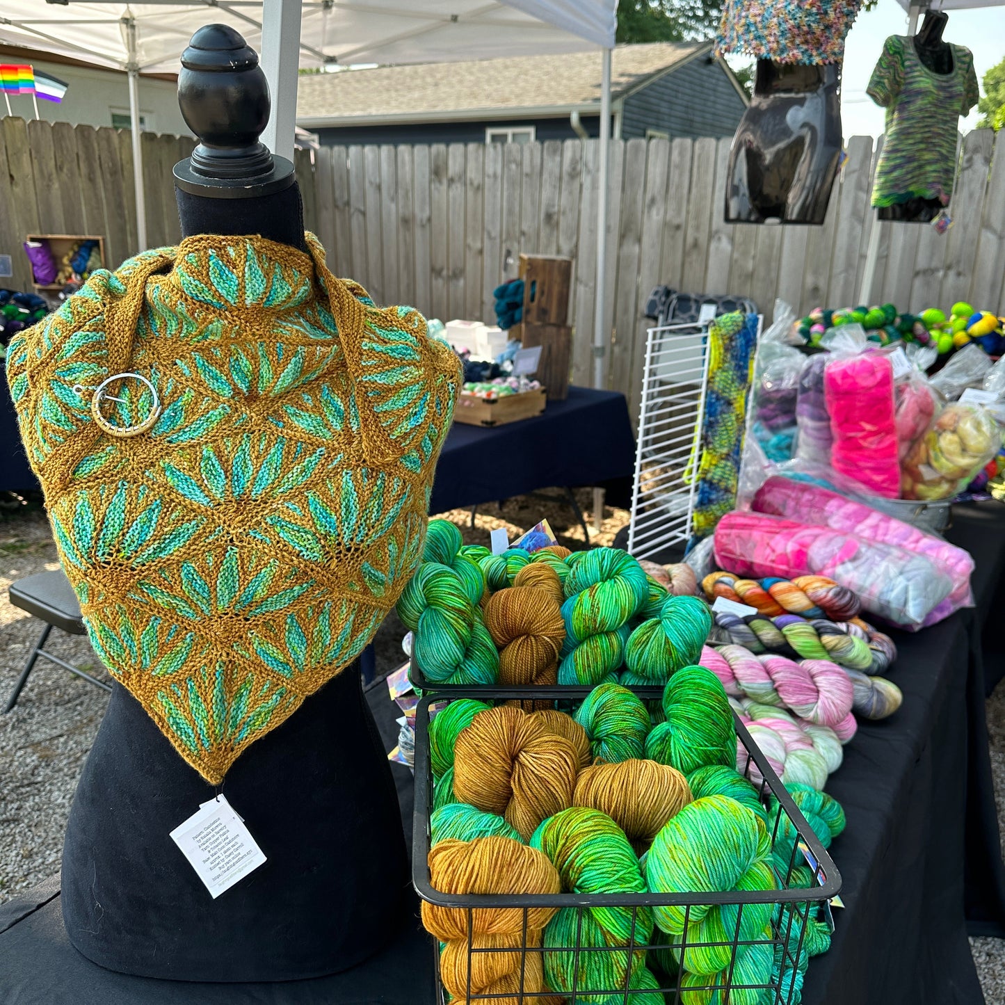 Knitted green and gold hat on a stand with yarn skeins in the background